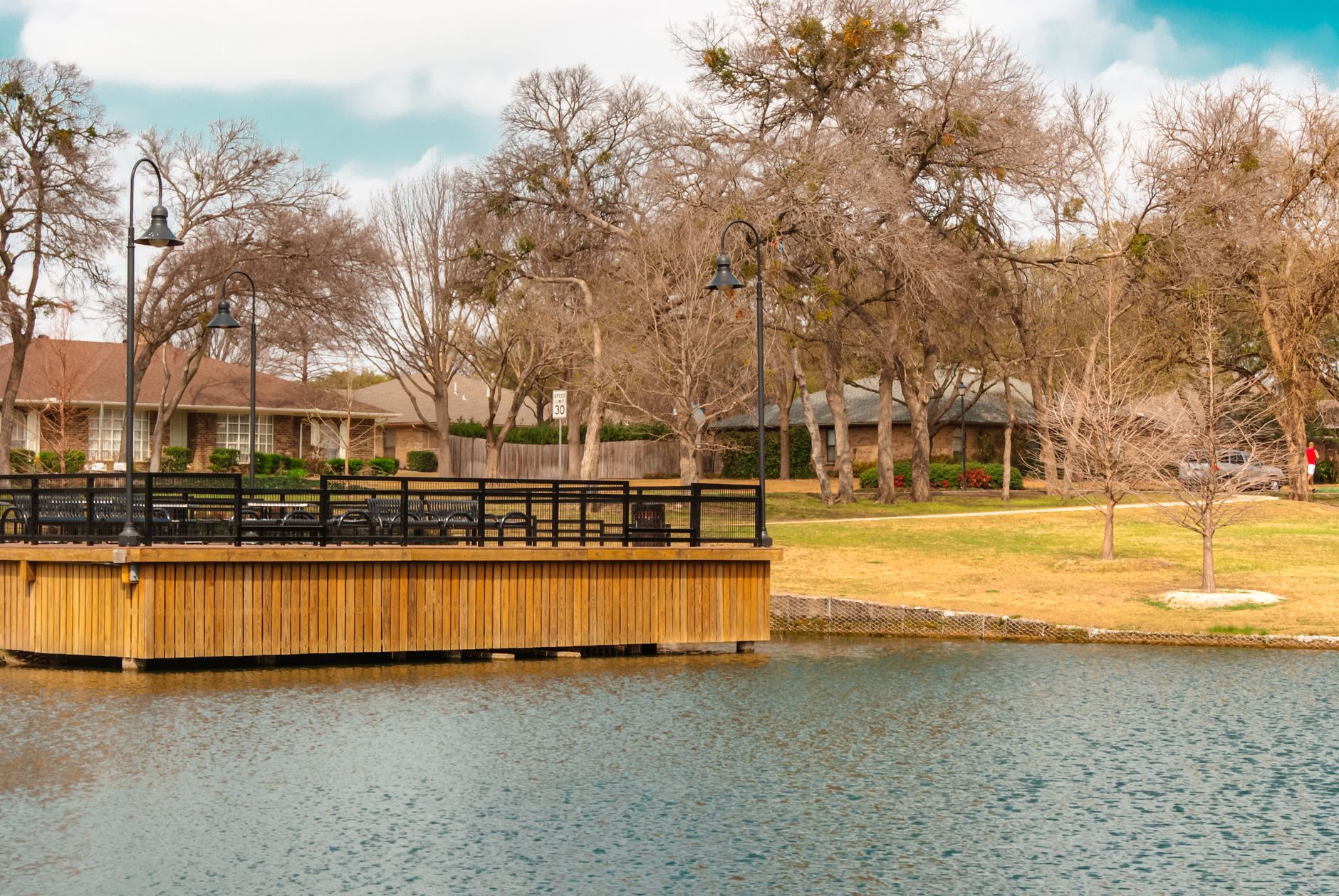 A tranquil lakeshore scene featuring a wooden platform, houses, and trees.