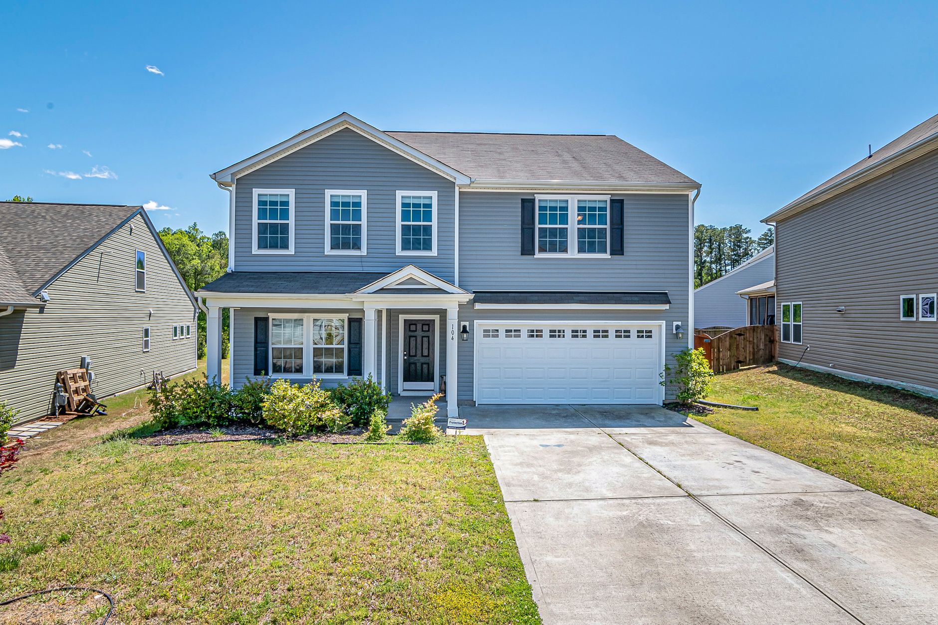 A modern two-story house with a large driveway and landscaped front yard under clear blue skies.