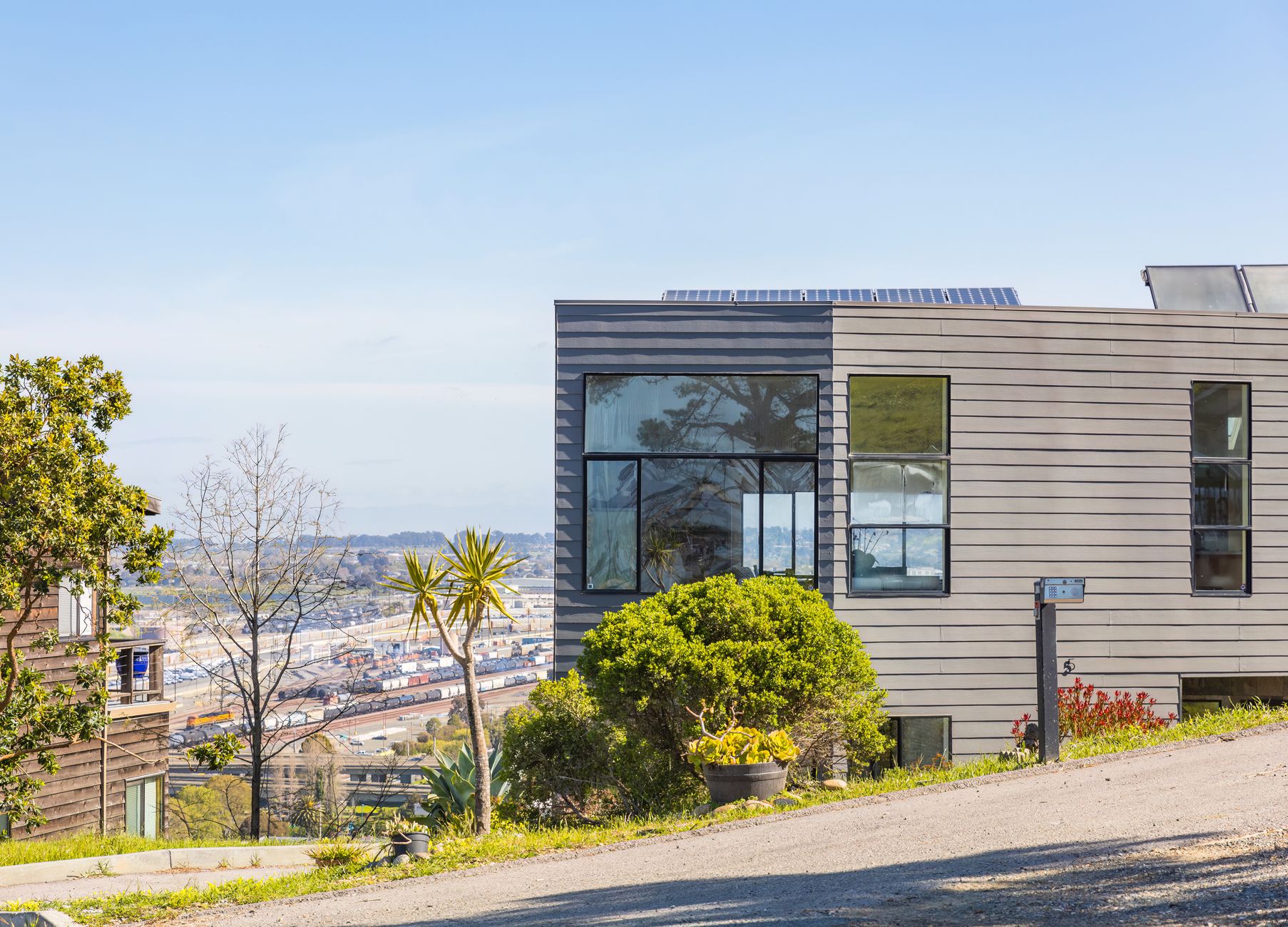 Contemporary house with large windows on a hill, overlooking cityscape under clear blue sky.