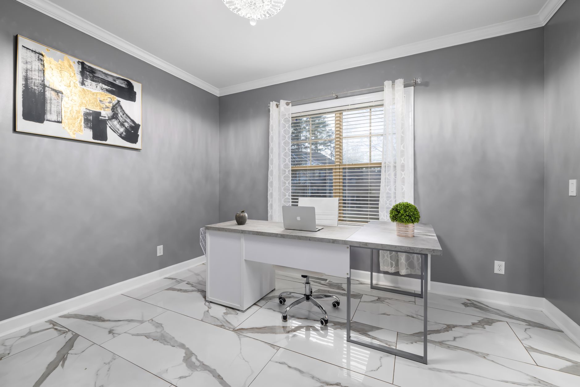 A spacious modern office with gray walls, marble flooring, and sleek furnishings, featuring a laptop and artwork.