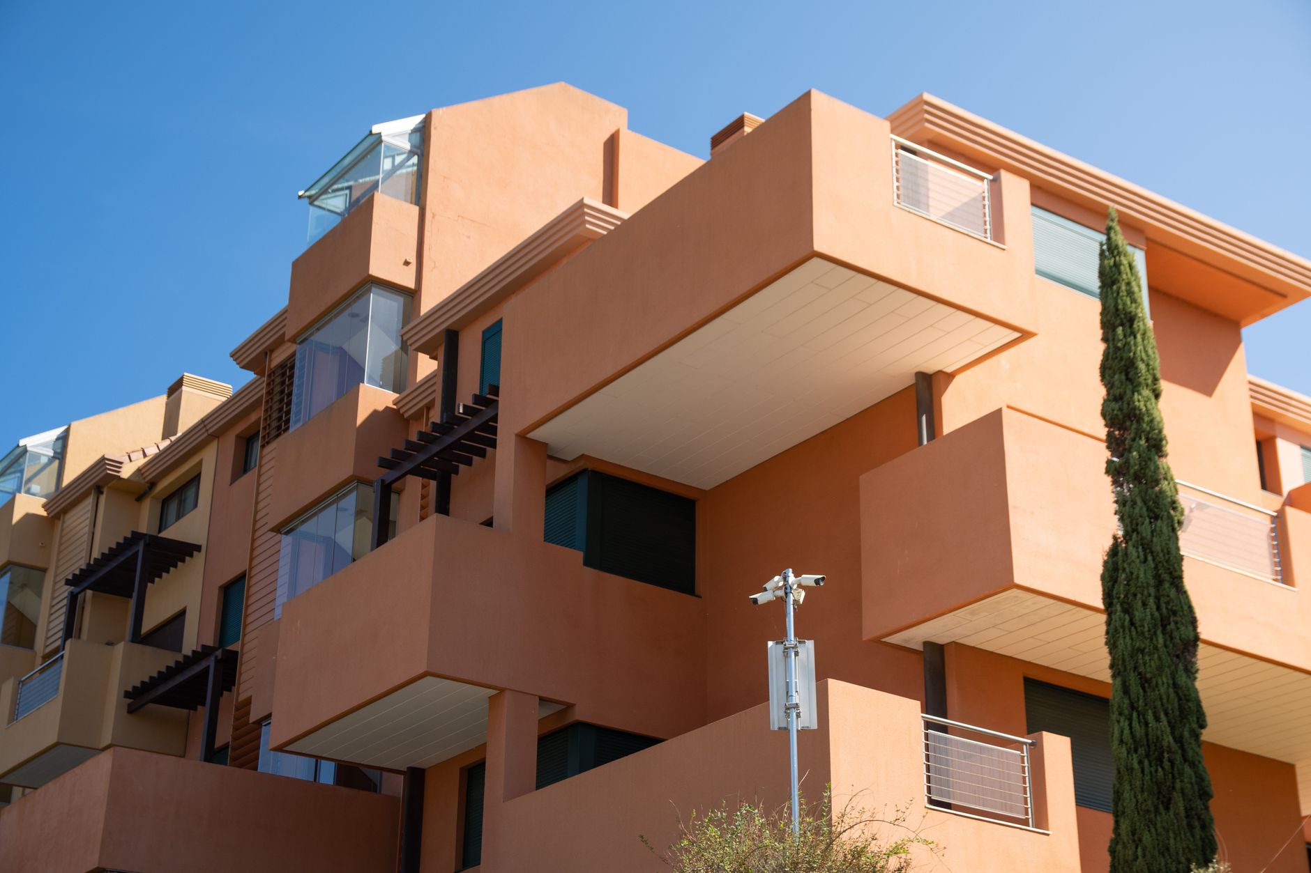Low-angle view of a modern building featuring geometric shapes and warm colors against a clear blue sky.