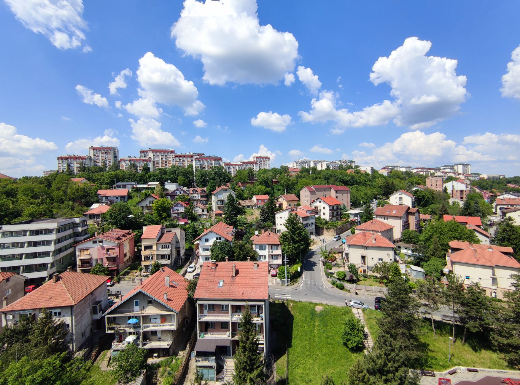 A scenic aerial view of a picturesque hillside neighborhood with lush greenery and vibrant rooftops under a clear blue sky.