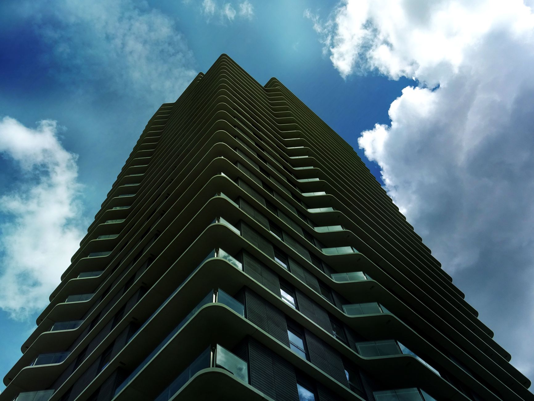 Low angle view of a modern skyscraper with glass facade against a cloudy blue sky.