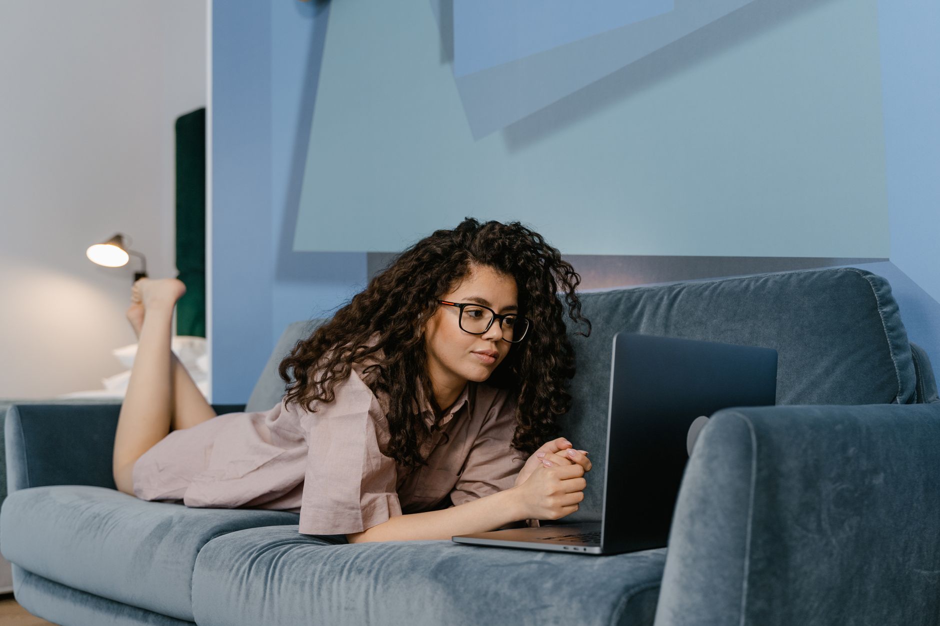 Woman in contemporary living room relaxed on sofa using her laptop for remote work.