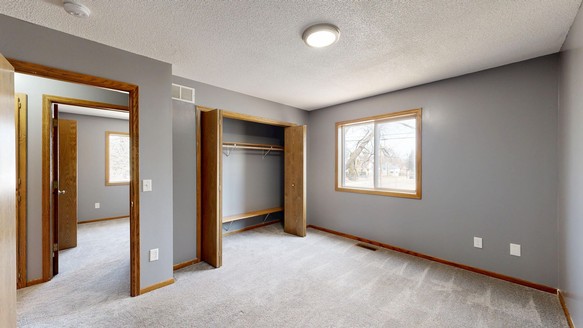 Spacious empty room with an open closet and window letting in natural light.