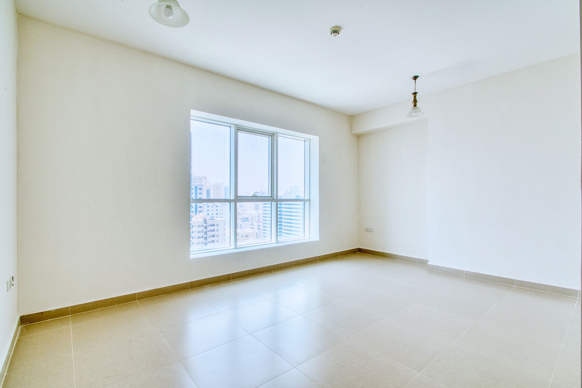 Spacious unfurnished apartment with large windows and natural light overlooking cityscape.