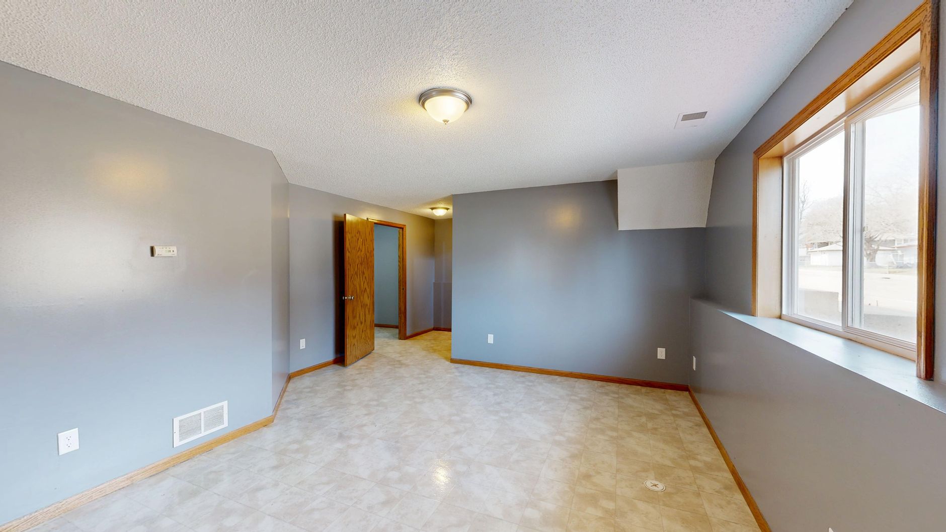 Spacious, light-filled empty room with gray walls and open wooden door.