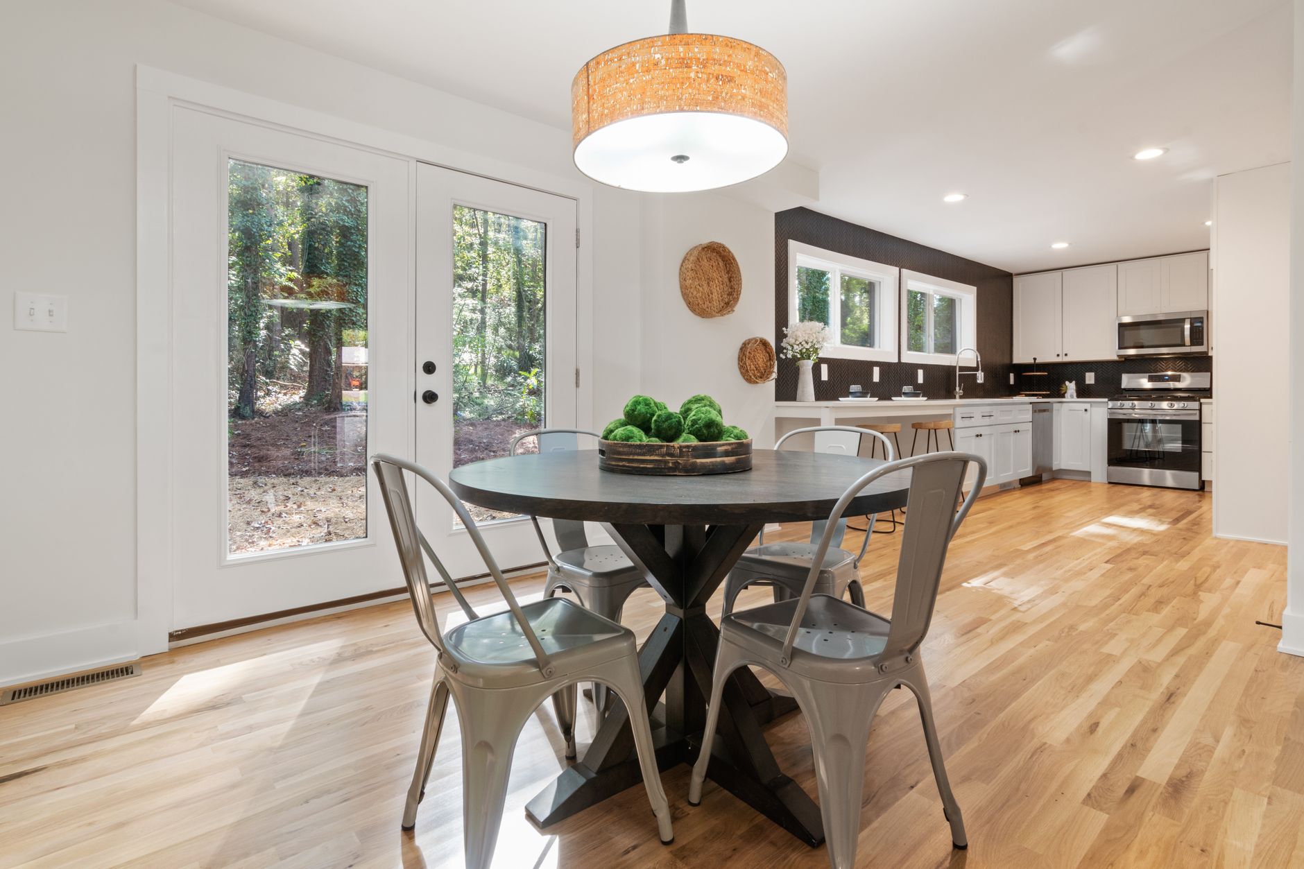 Bright dining area with wooden flooring and kitchen view, open to nature.