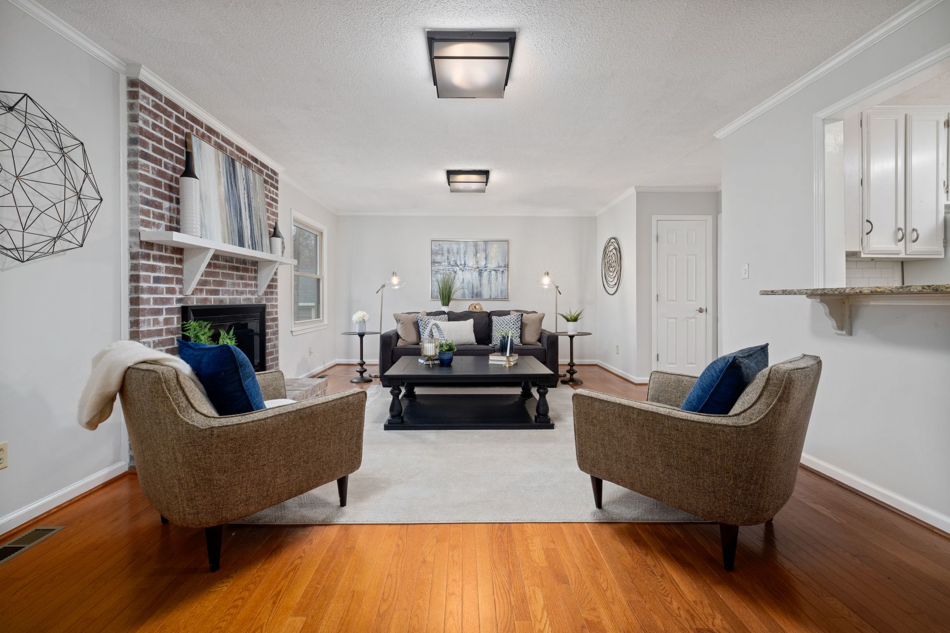 A spacious modern living room featuring a brick fireplace, elegant armchairs, and contemporary decor.