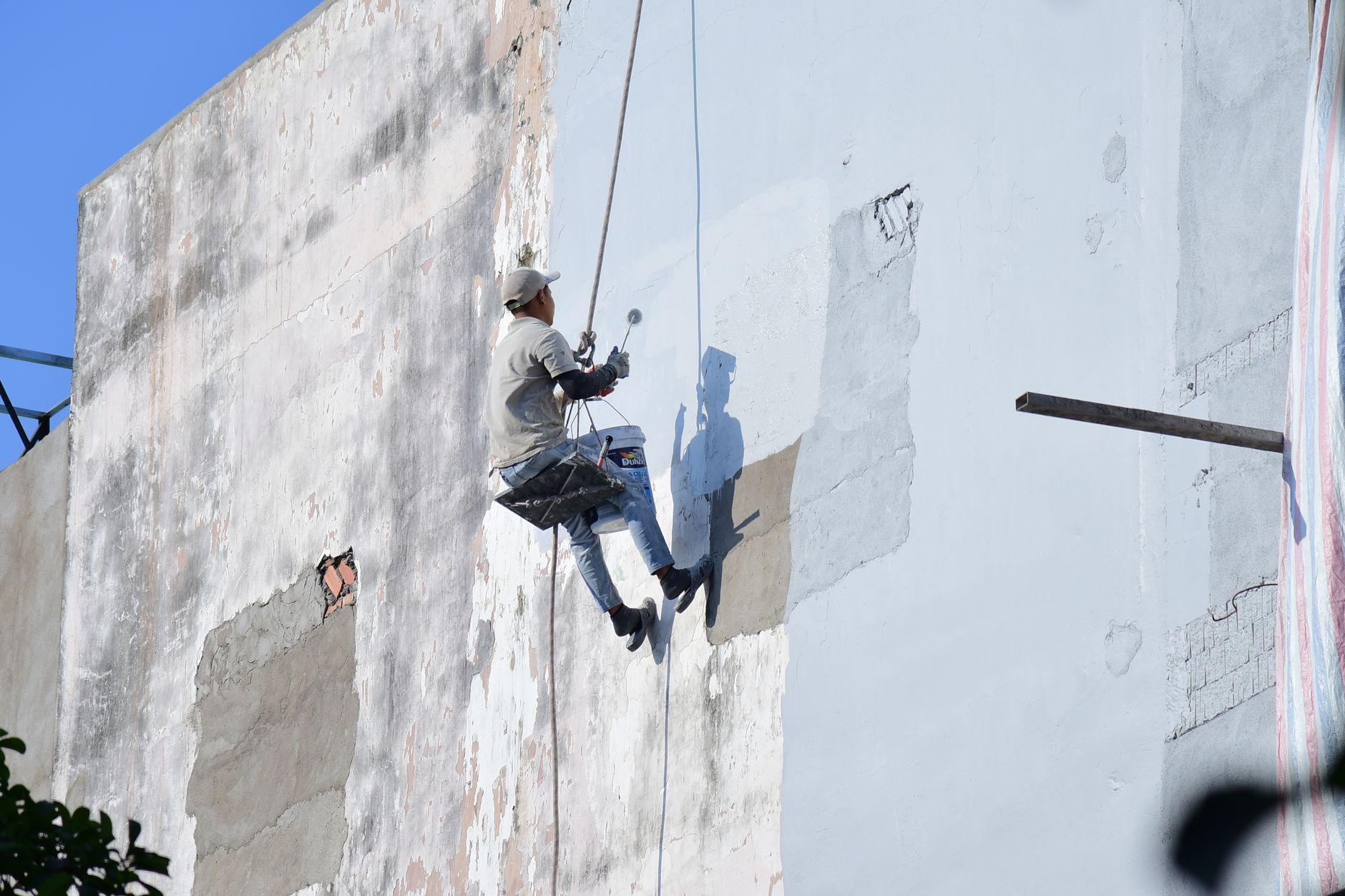 A rope access worker suspended while painting a high-rise building facade.