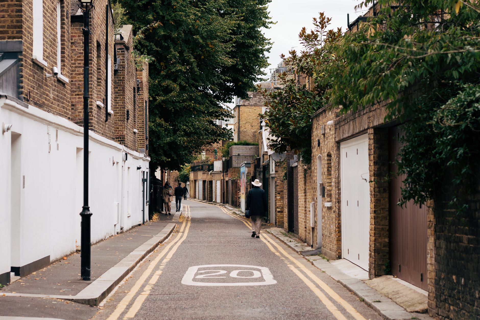 A quiet London street with brick houses, lush greenery, and a pedestrian walking.