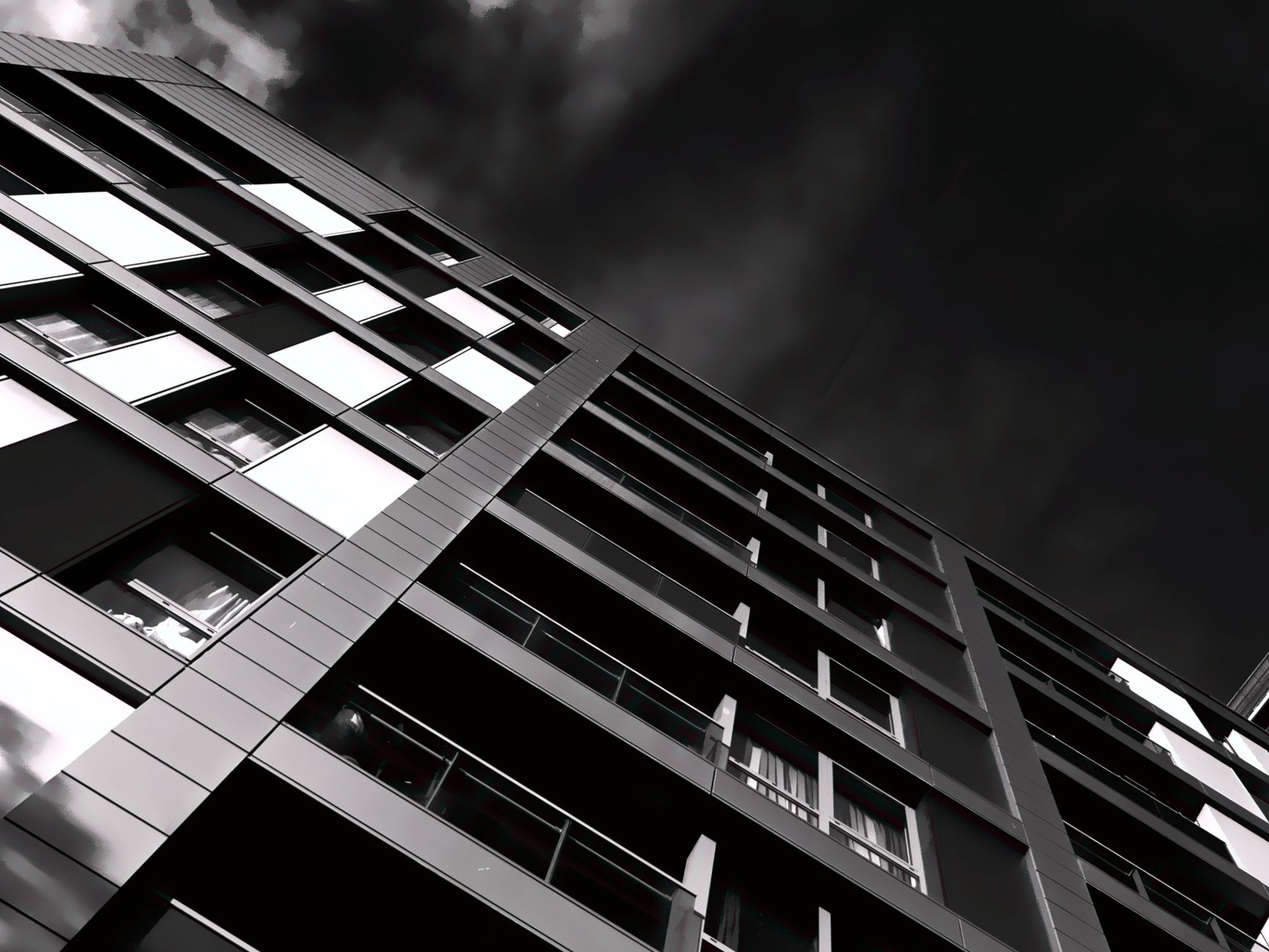 A striking black and white image capturing the low angle of a modern building with a dramatic sky.