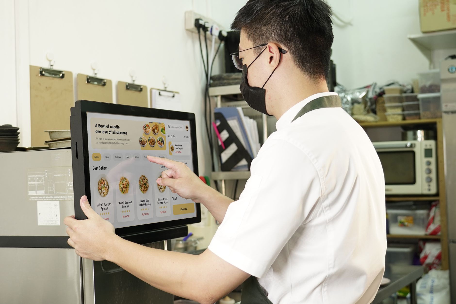 A restaurant worker interacts with a digital touchscreen menu in the kitchen.