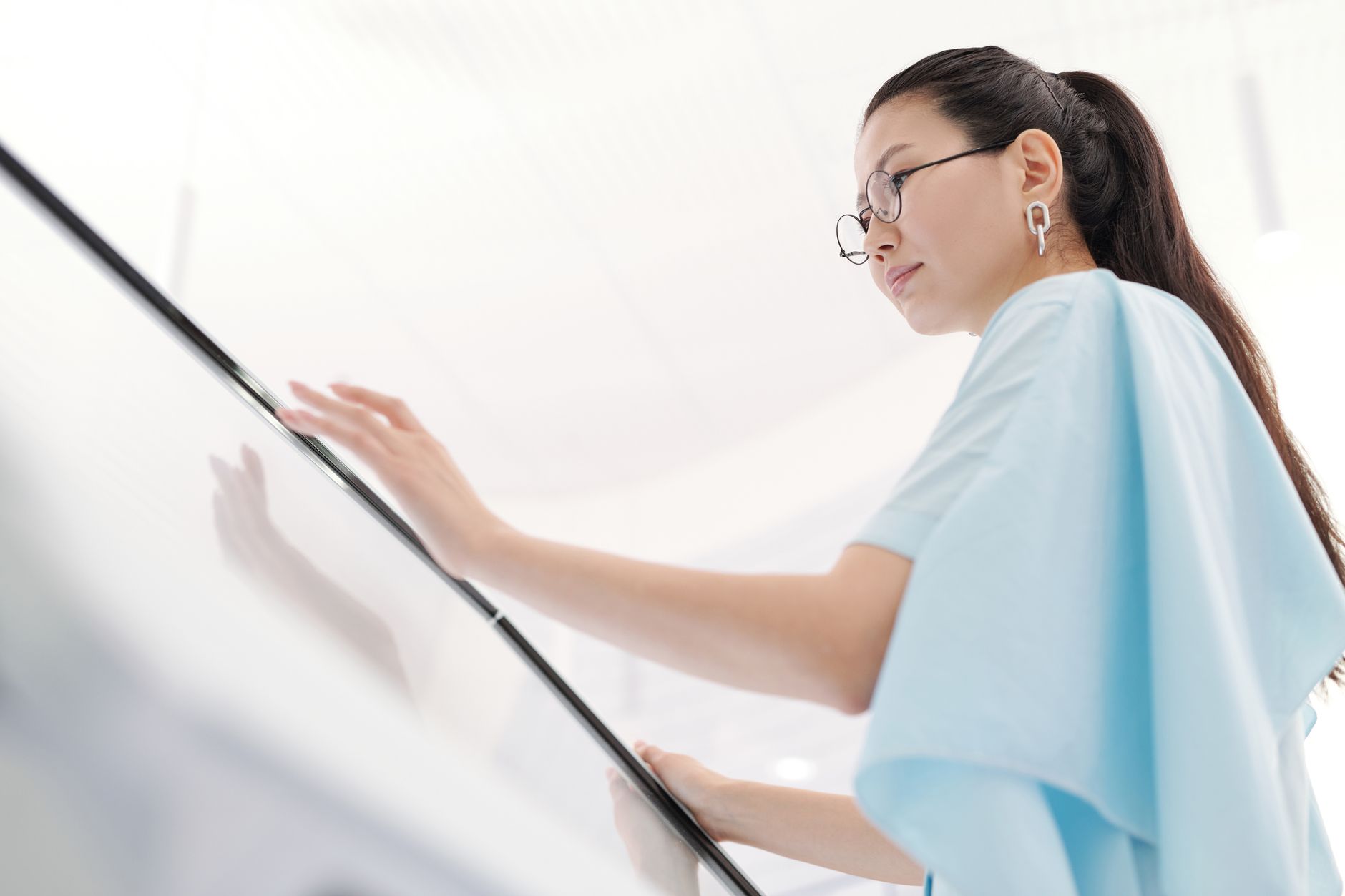 Asian woman in glasses engaging with a touchscreen in a modern indoor setting.