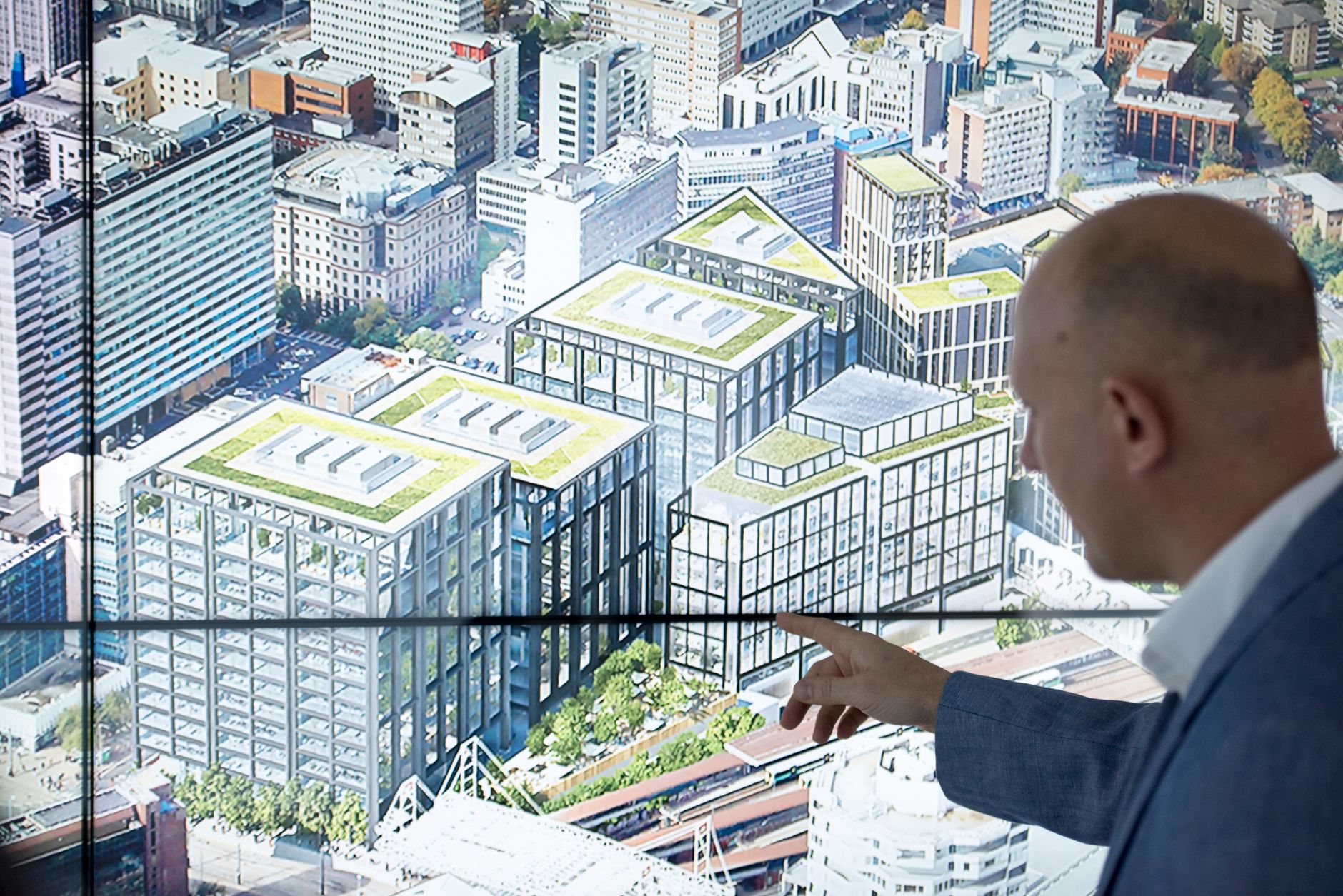 Businessman pointing at a cityscape diagram on a touchscreen, showcasing modern urban planning.