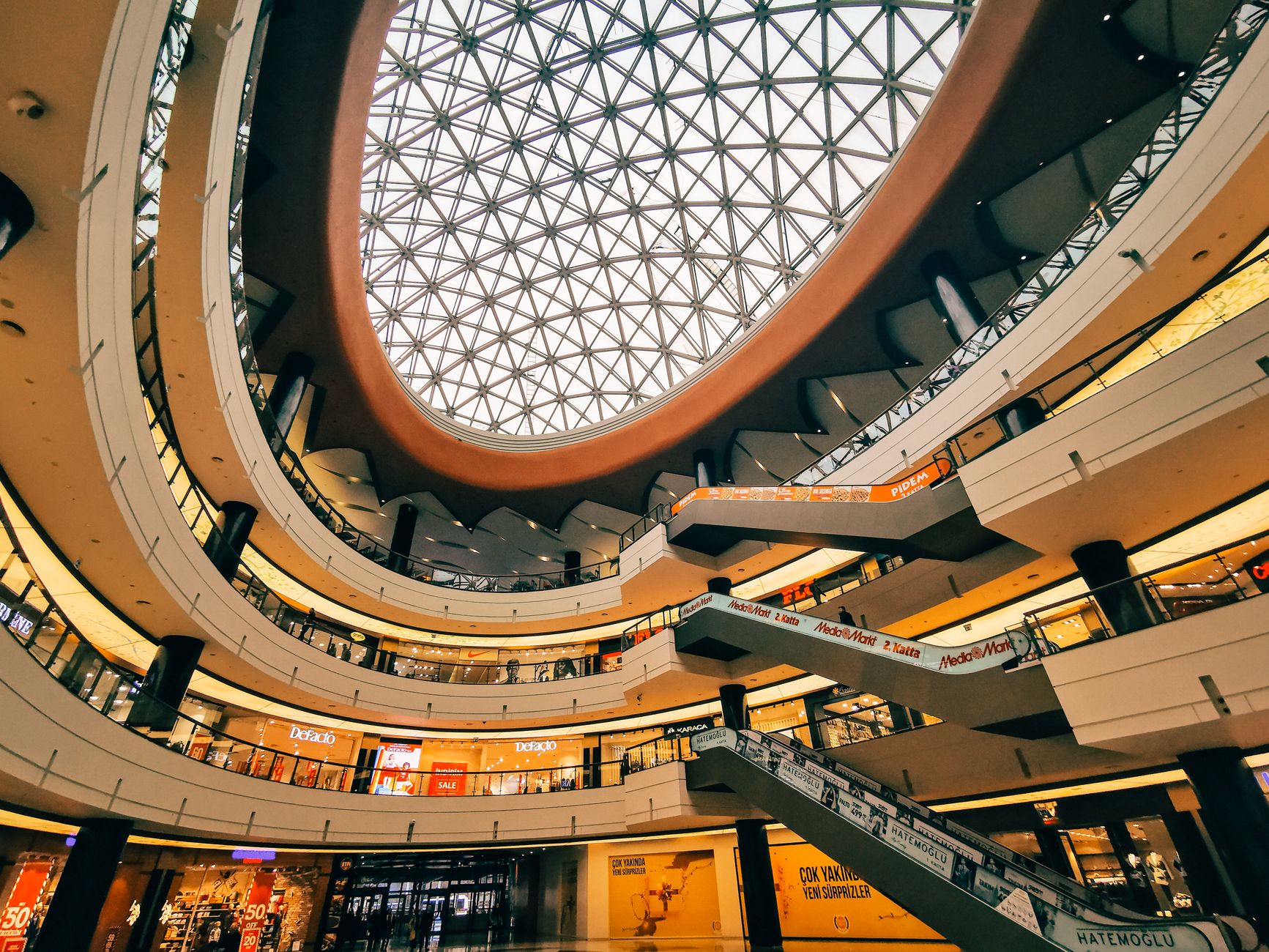 Wide-angle view of a futuristic shopping mall interior featuring a geometric glass ceiling and multiple levels.