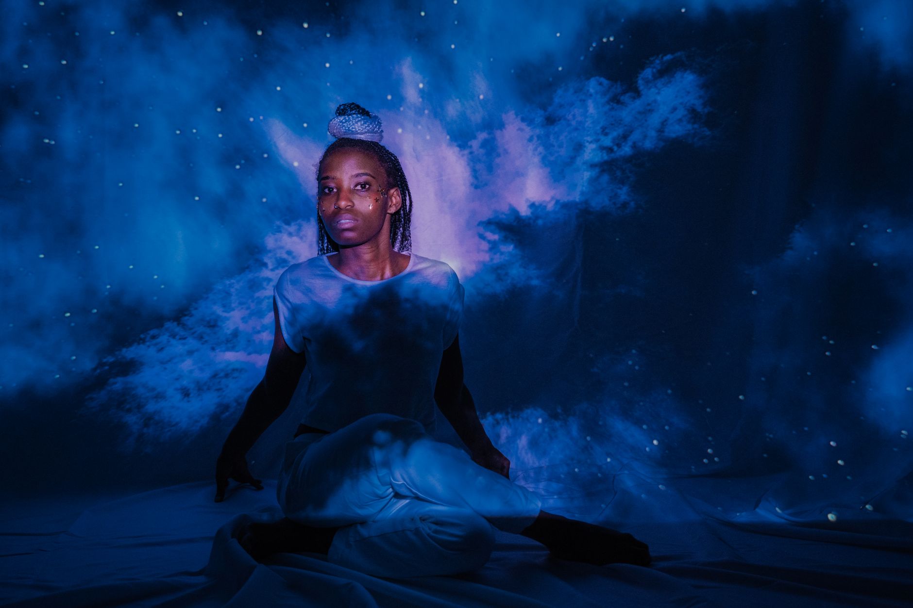 A woman seated with ethereal projections creates a dreamy celestial scene.