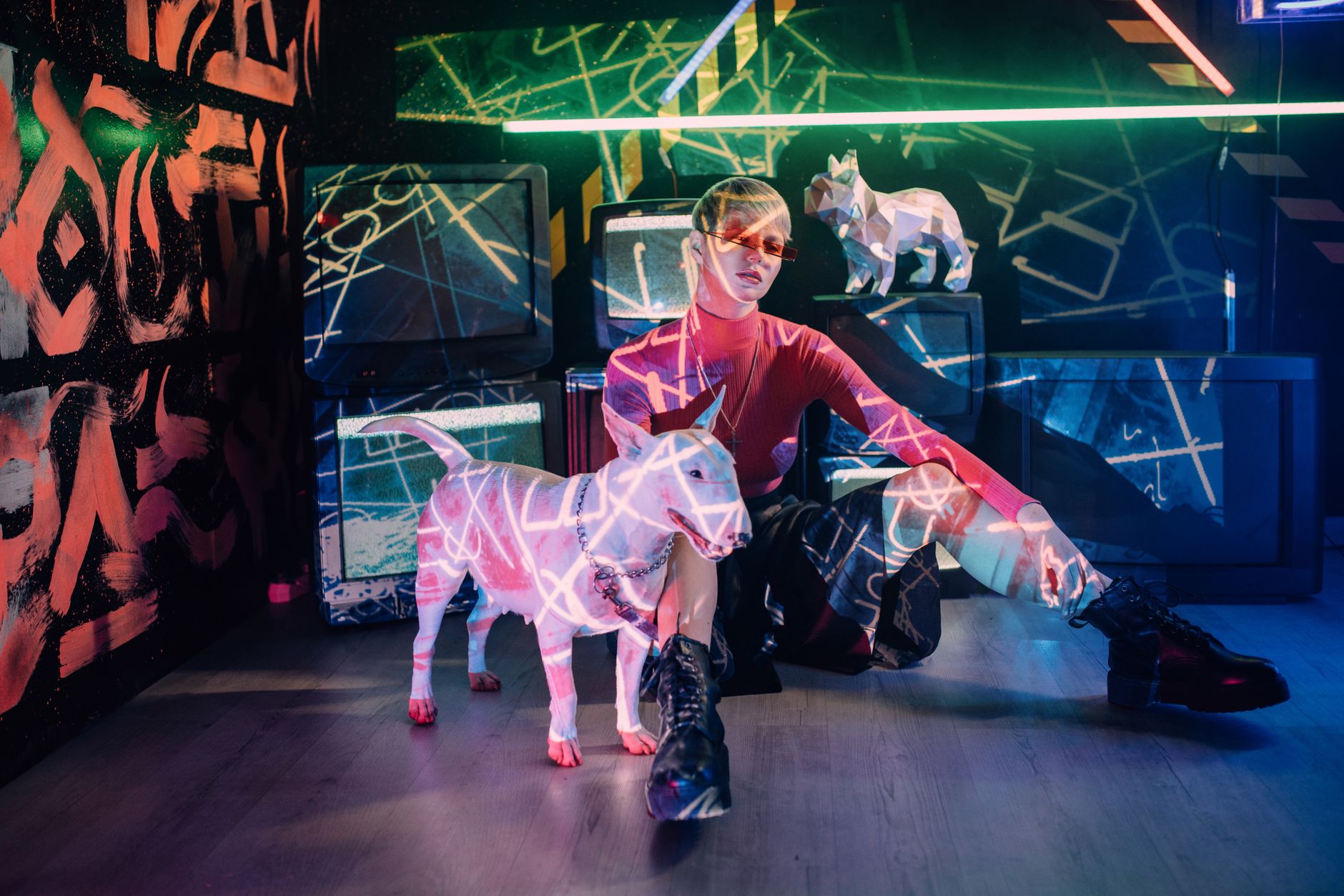 A woman and a dog sit in a neon-lit art studio with colorful light projections.