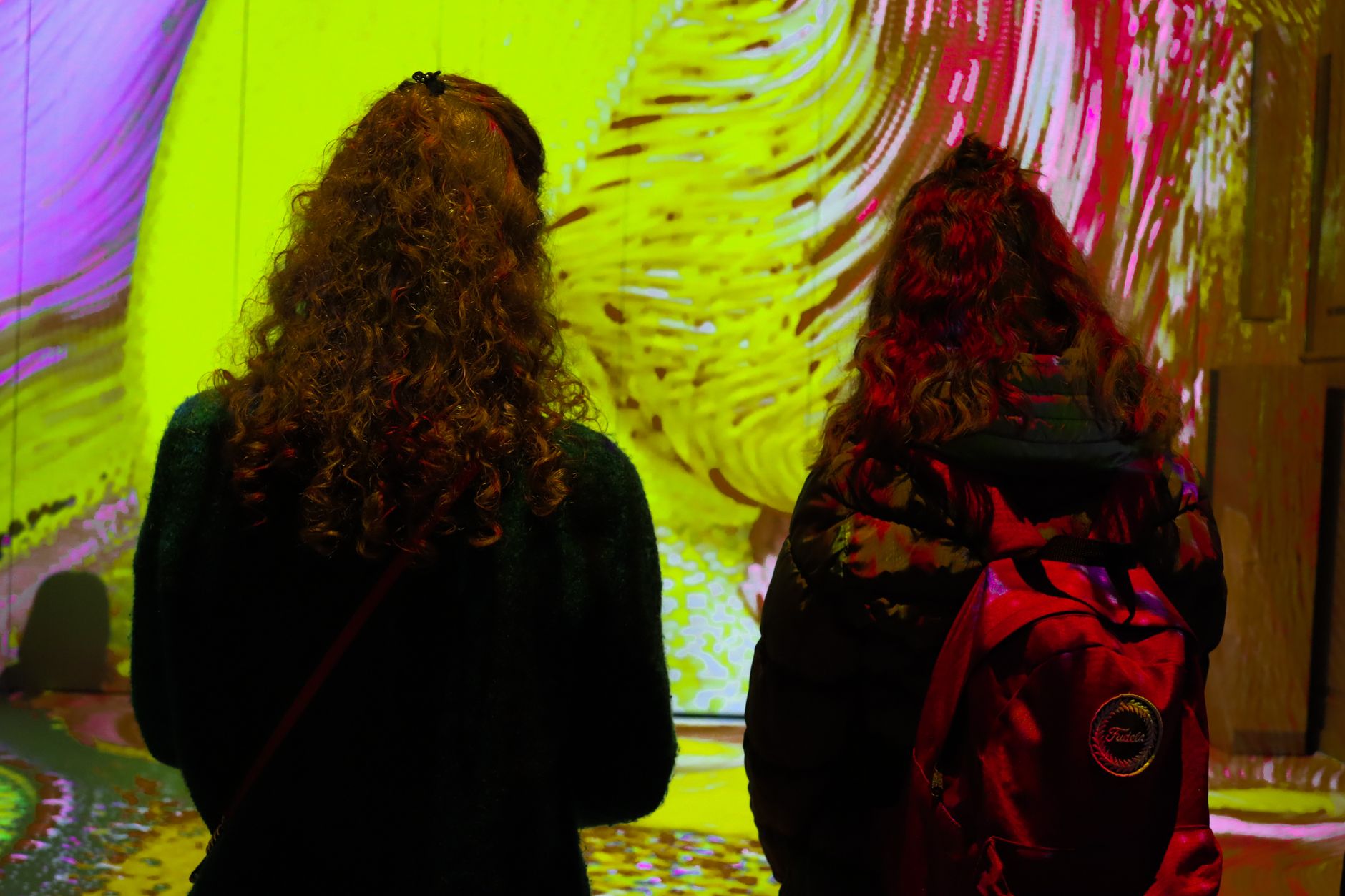 Two women with curly hair observe colorful projections in an art gallery.