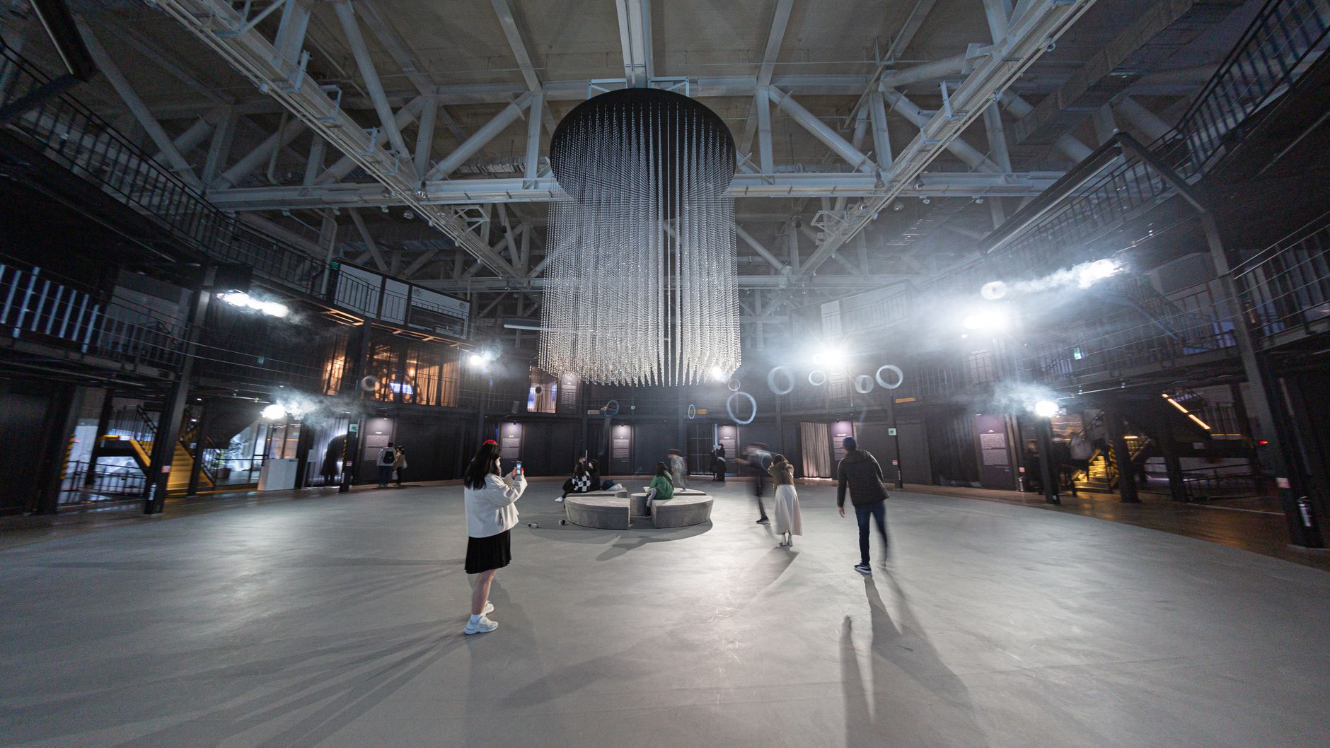 Spacious contemporary hall with modern chandelier and people exploring the urban architectural interior.