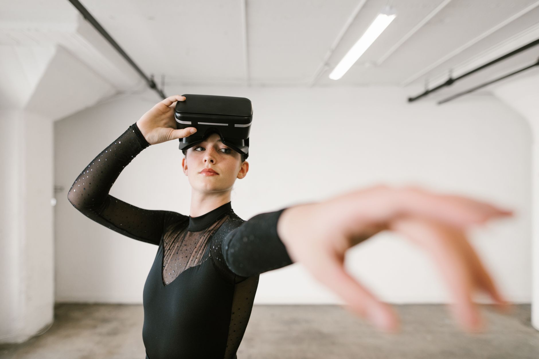 Dancer in a black leotard using VR goggles and posing gracefully indoors.