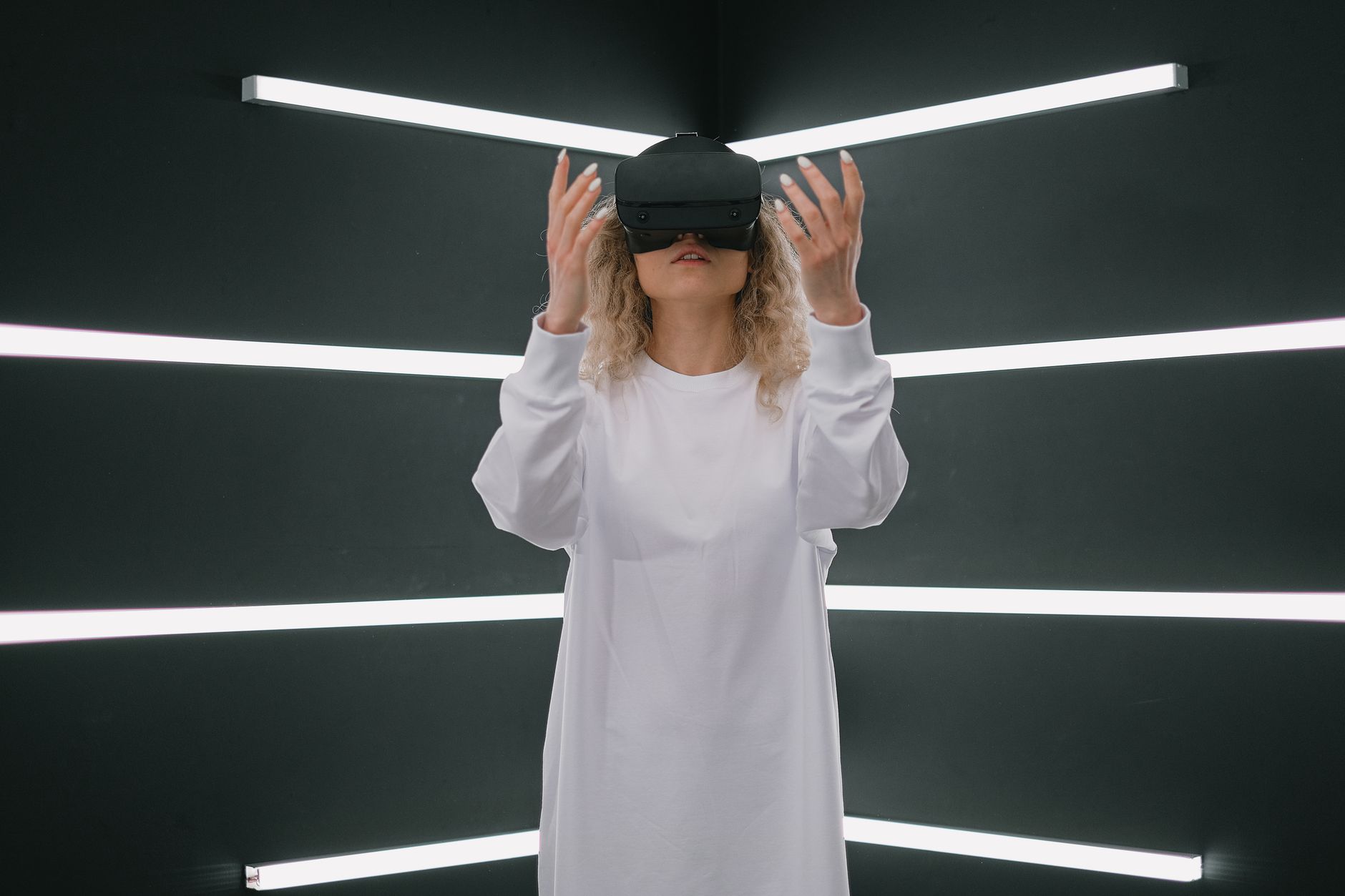 A woman in a white dress explores virtual reality with a VR headset in a modern, futuristic setting.