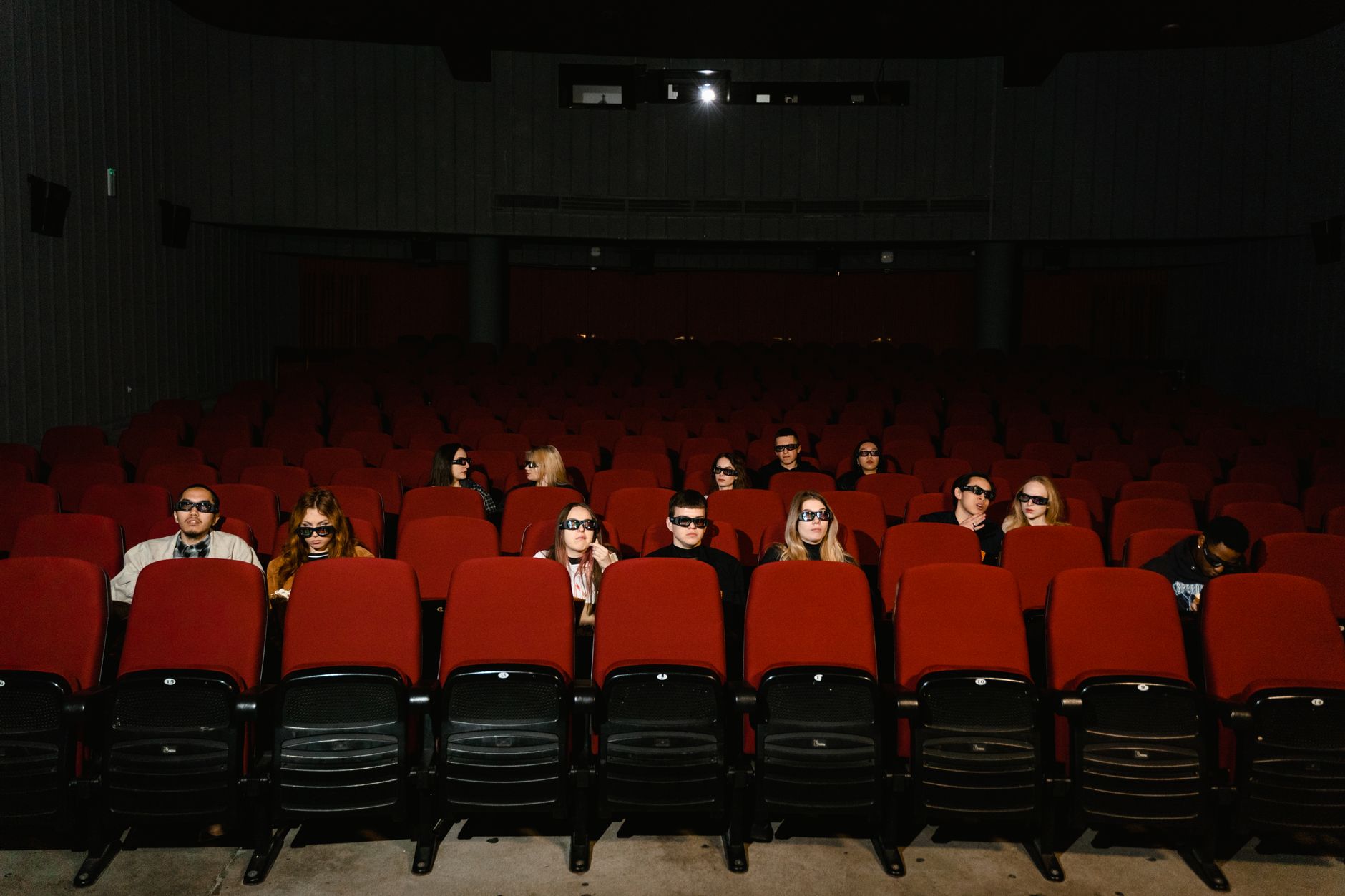 People watching a movie wearing 3D glasses in a near-empty cinema hall.