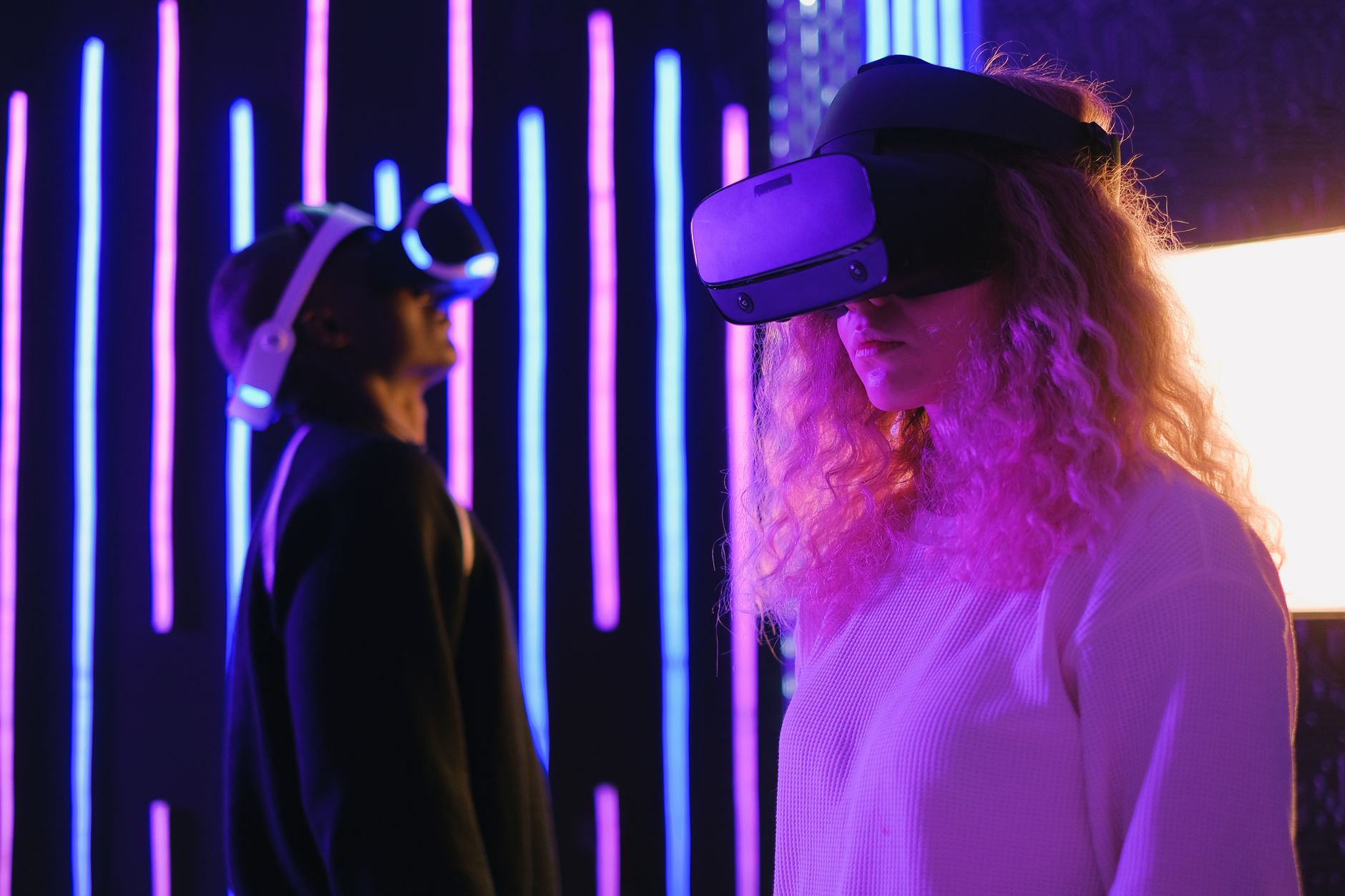 Two young adults engaged in a virtual reality experience with VR headsets in a neon-lit environment.