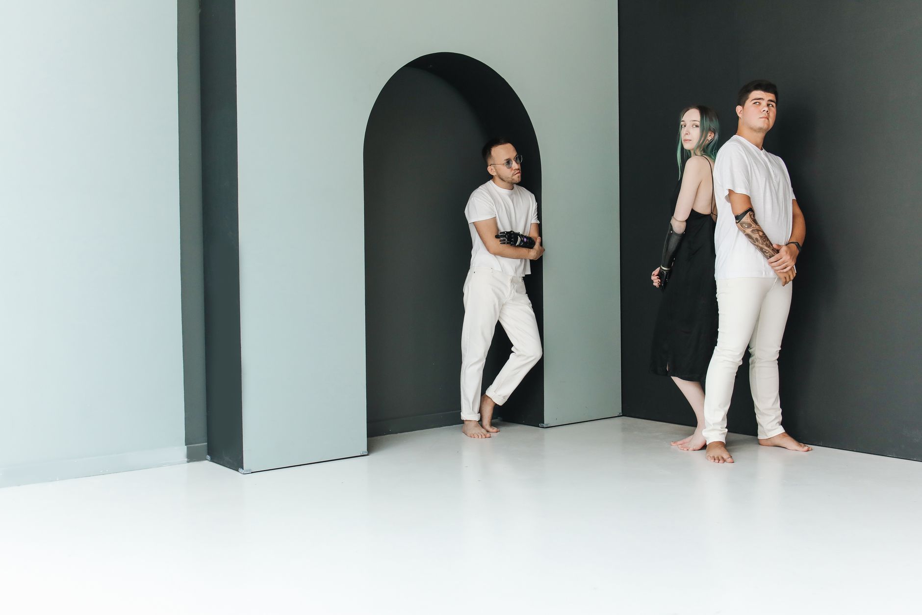 Three diverse individuals in minimalist studio with prosthetic elements.