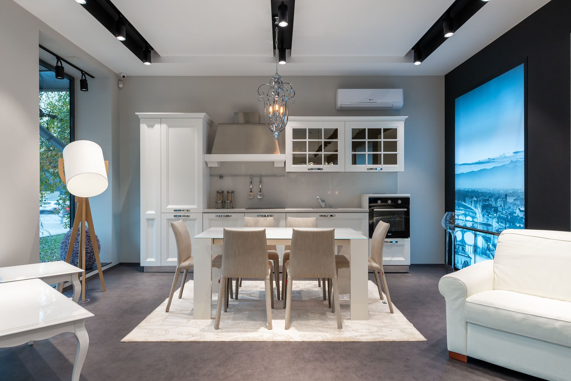 Chairs at table placed on rug near white cupboards and modern appliances at stylish kitchen with window and glowing lamp