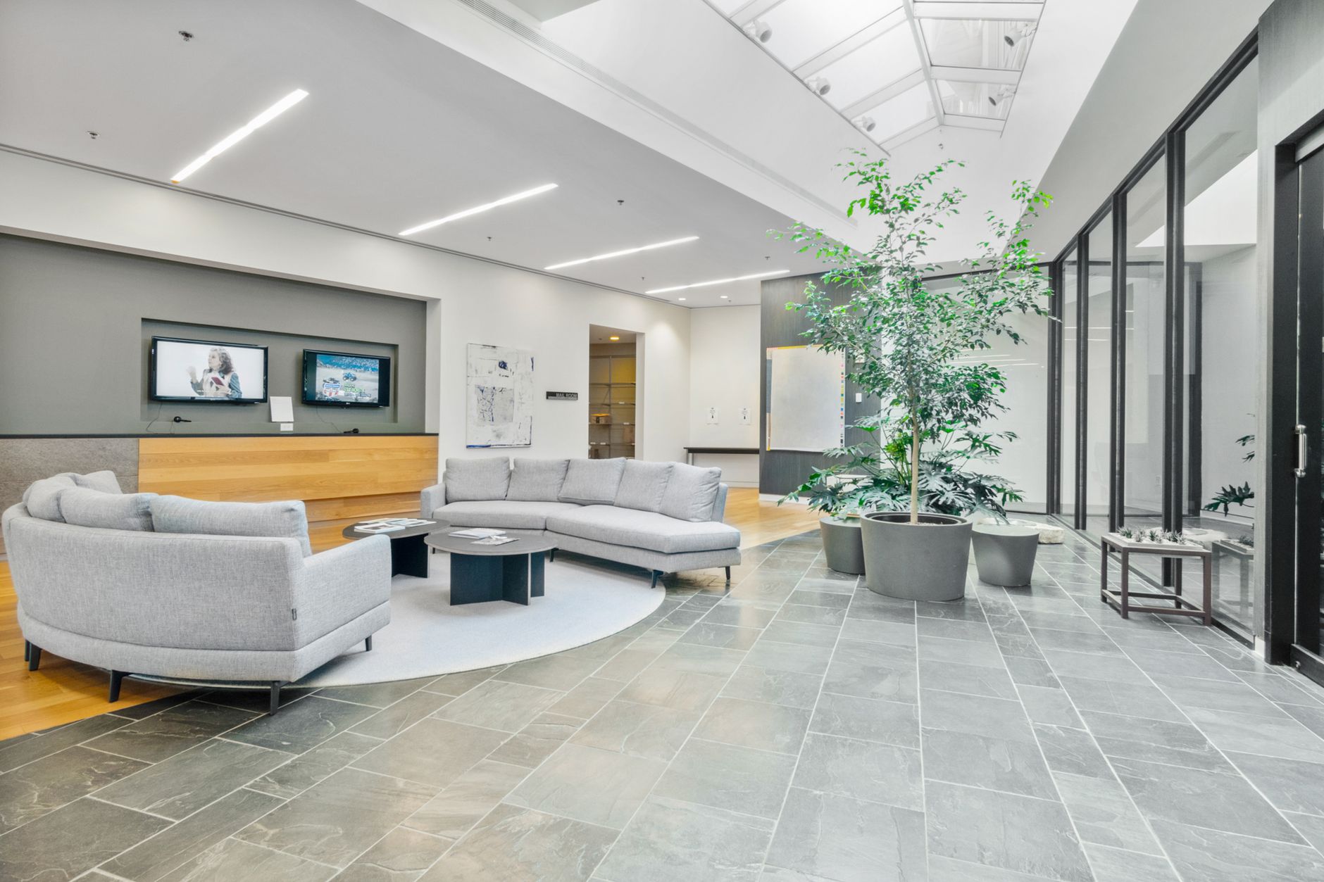 Spacious office lobby featuring gray sofas, potted plants, and bright lighting. Ideal for business spaces.