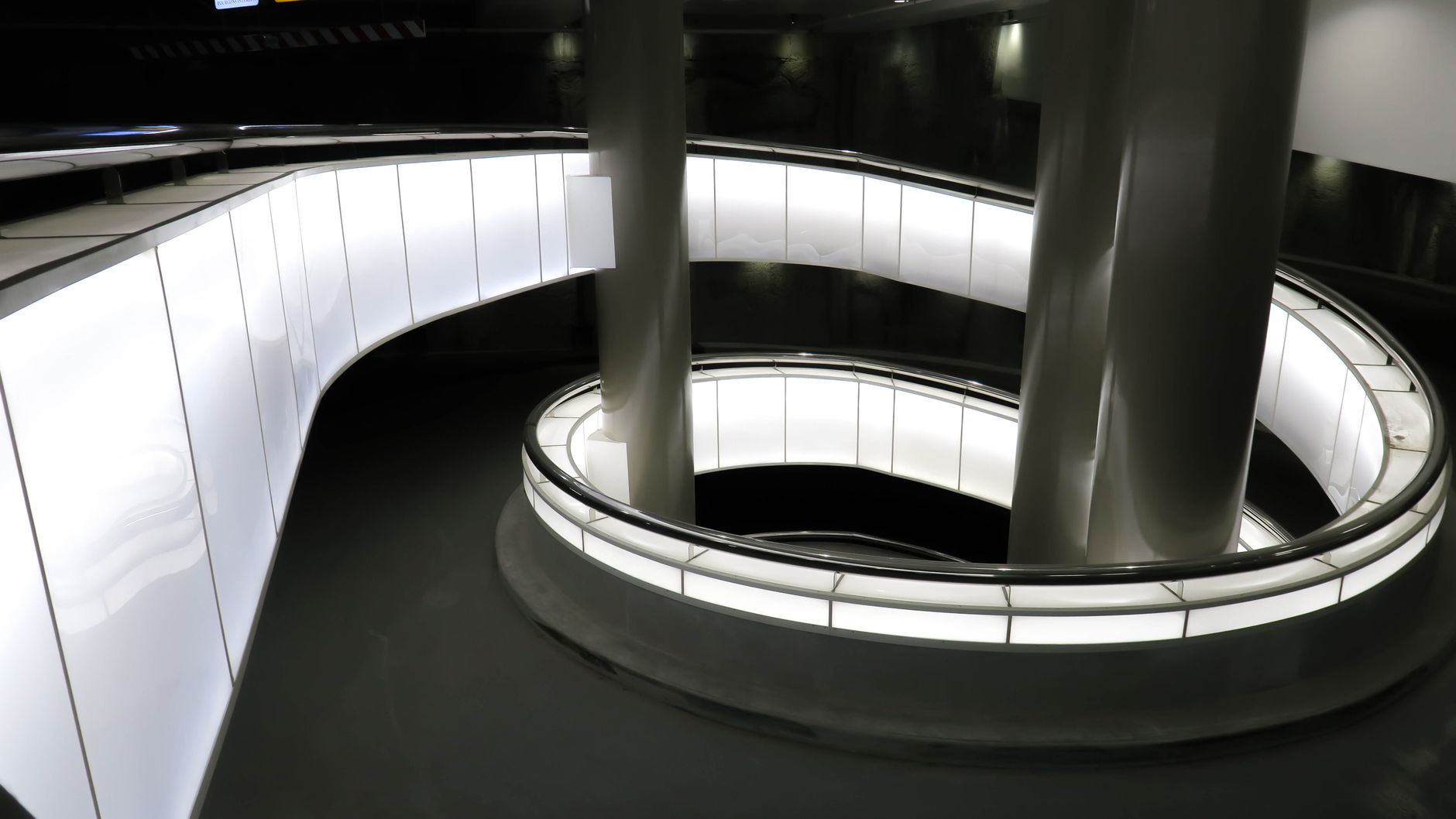 A modern spiral staircase highlighted by illuminated columns, showcasing sleek architectural design indoors.