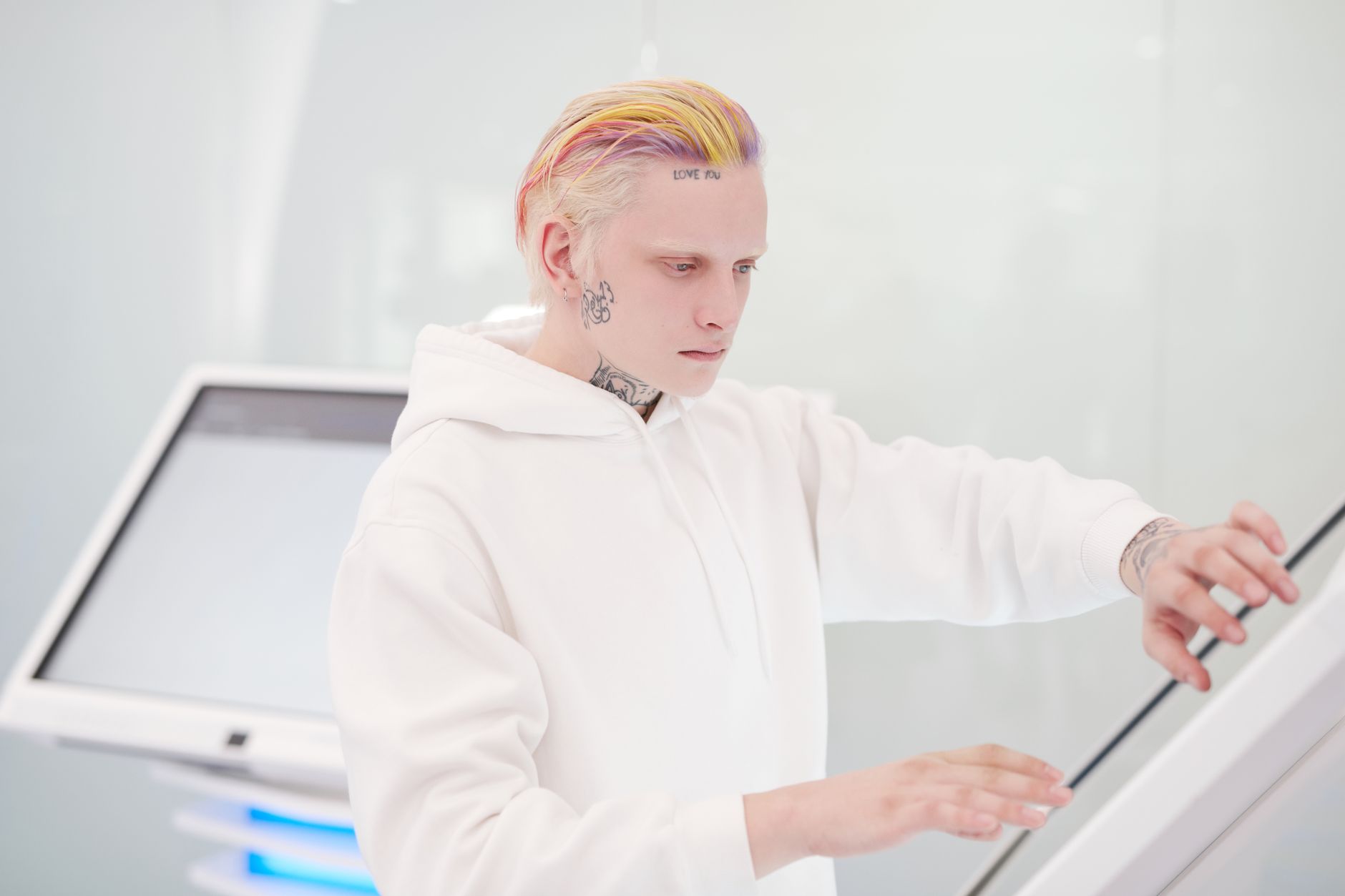 Portrait of a tattooed man with colored hair using a touchscreen kiosk in a modern setting.