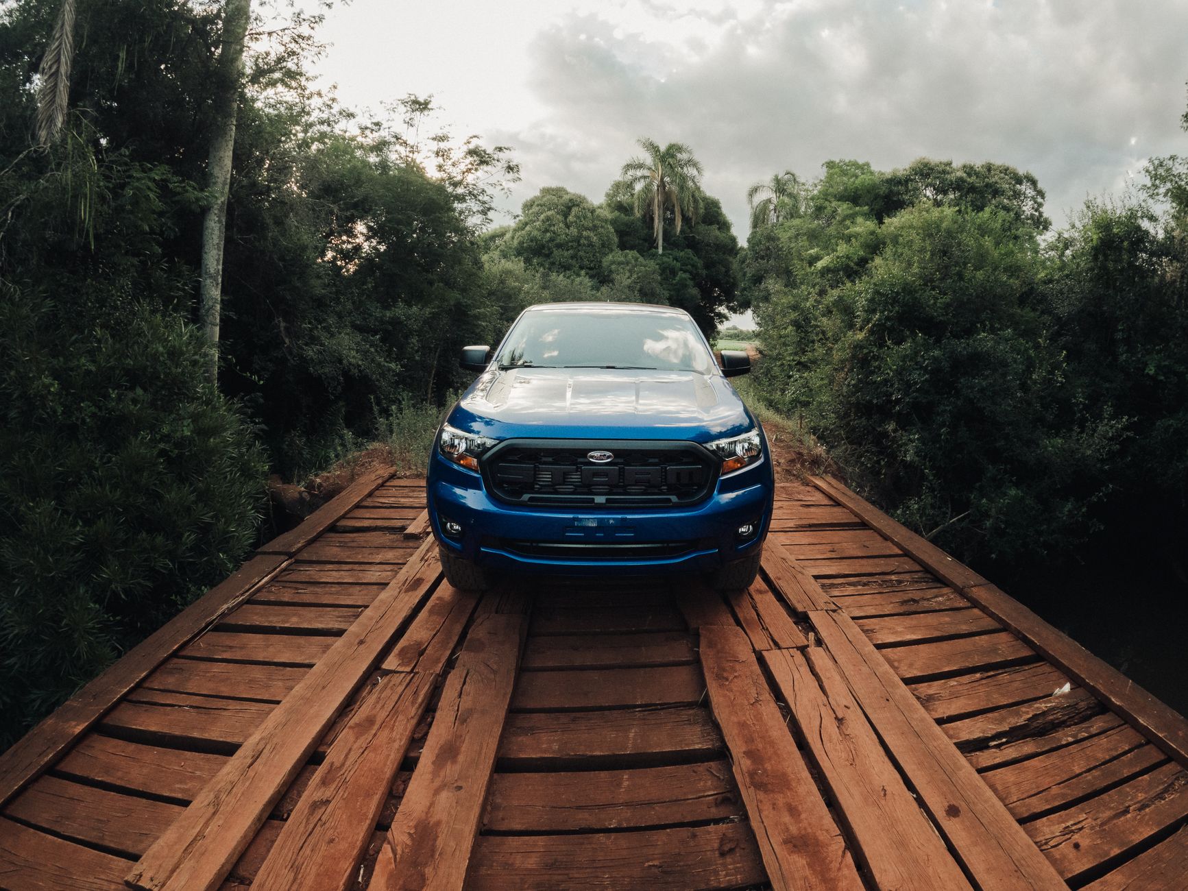 Blue SUV parked on a wooden bridge amidst lush greenery in Cruz Alta, Brazil.