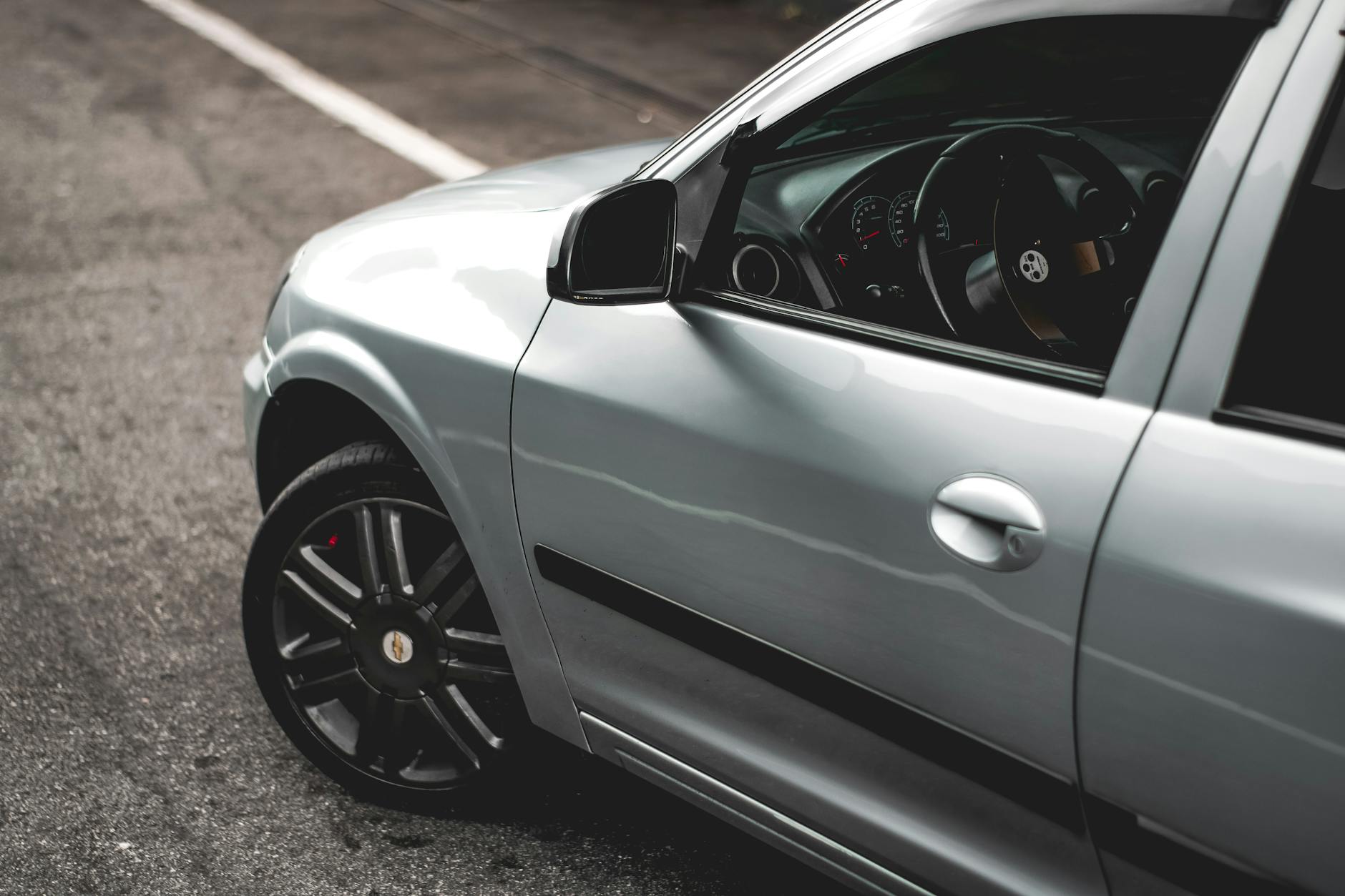 A detailed view of a silver car's side and interior in an urban environment, showcasing modern design.