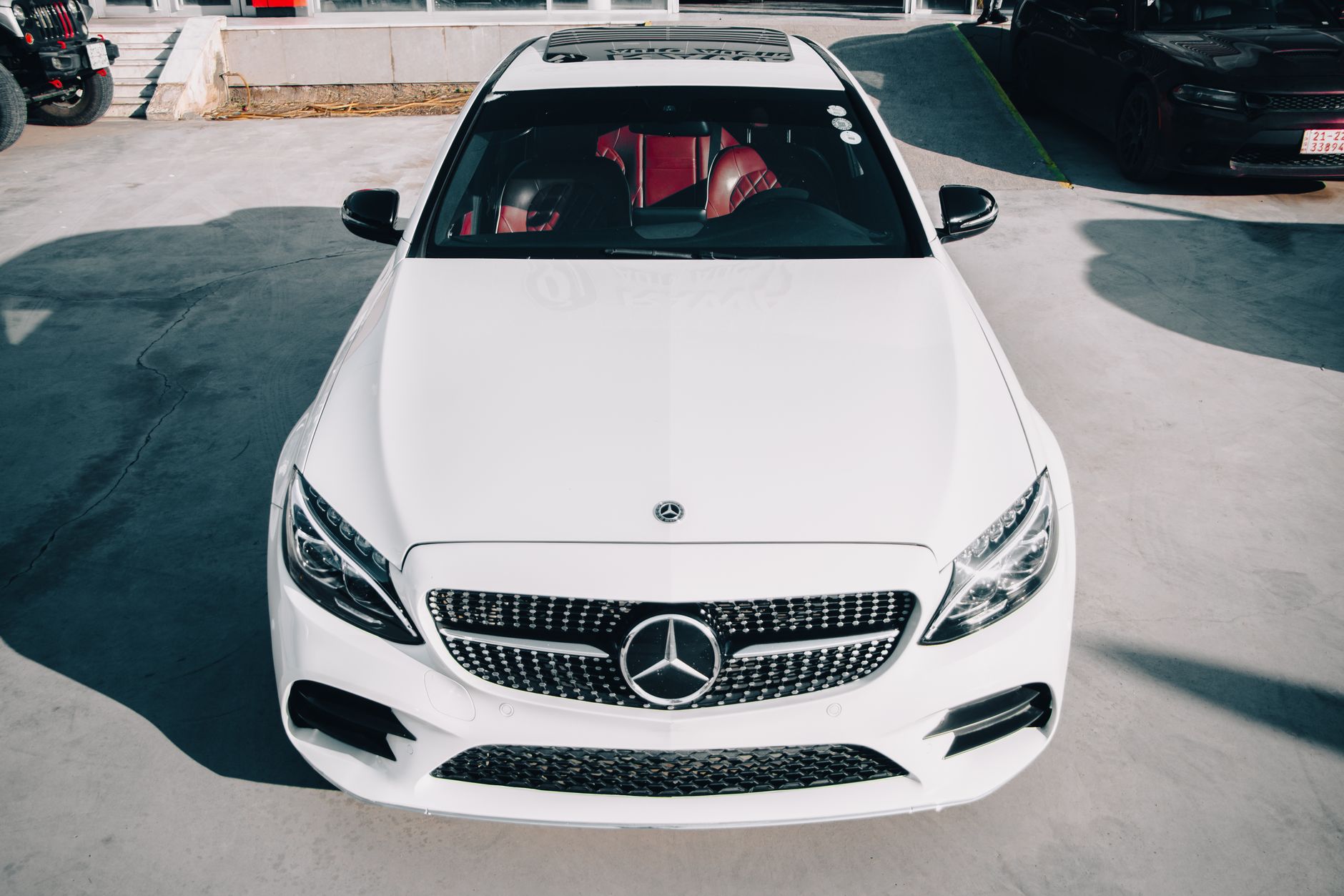 A high angle view of a white Mercedes Benz car in an outdoor sunlit parking area.