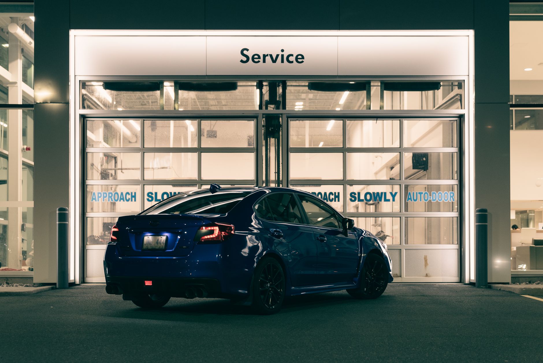 A sleek blue car parked at a service station entrance illuminated at night with modern lighting.