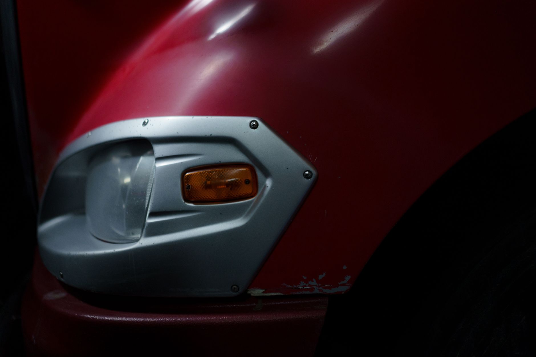 Detailed image of a red vehicle's headlight and chrome trim in a garage setting.