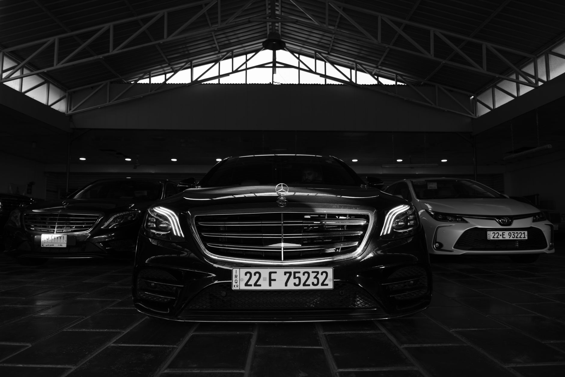 Black and white image of luxury cars in an indoor showroom with striking lighting.