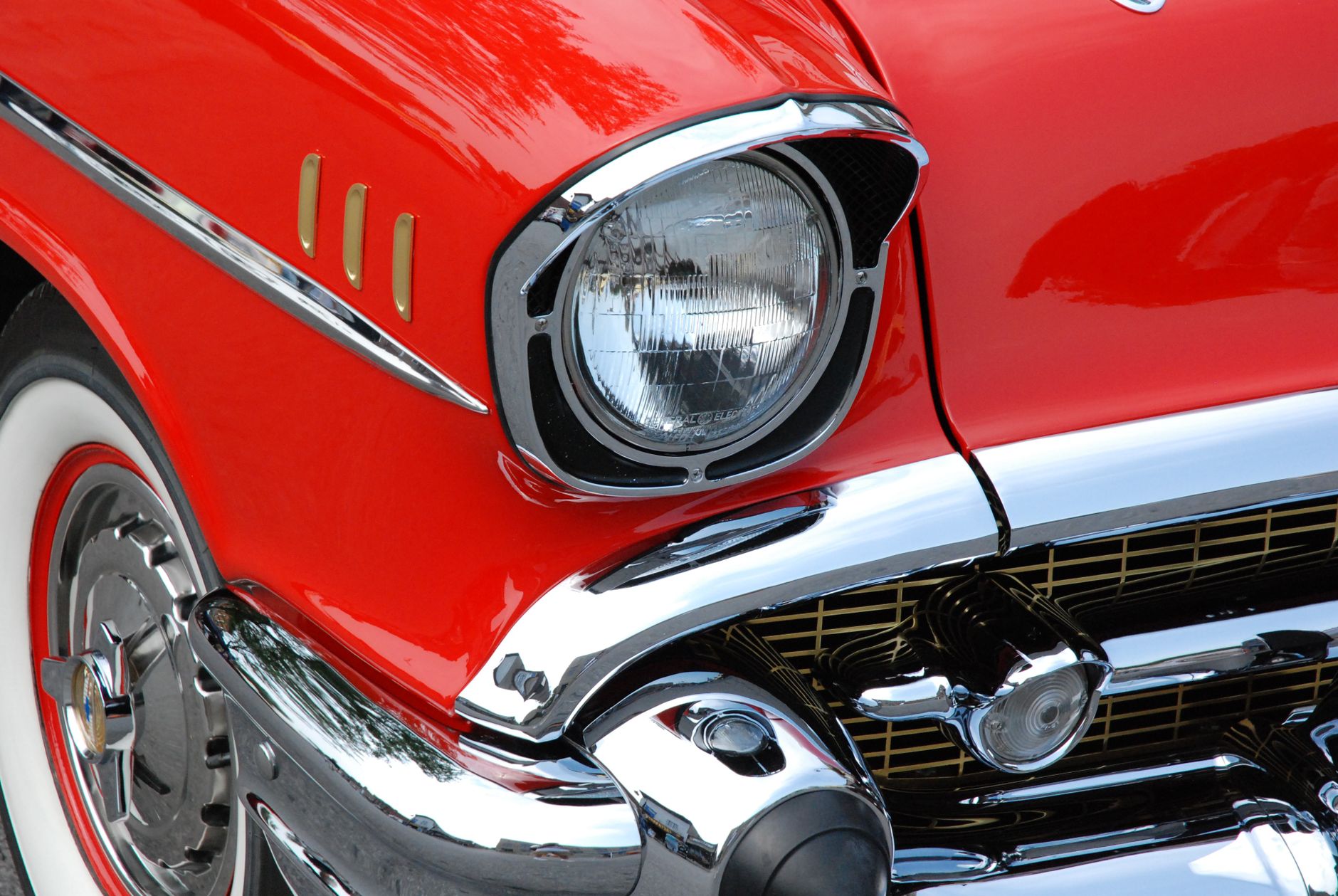 Detailed view of a red vintage car's front with chrome accents and whitewall tires.