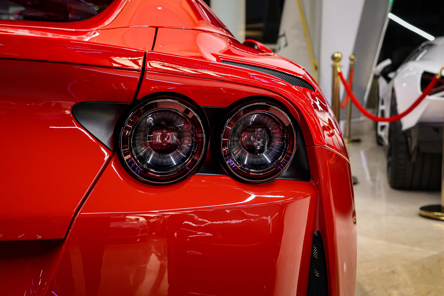 Close-up of a red luxury sports car's rear in a showroom with vibrant lighting.