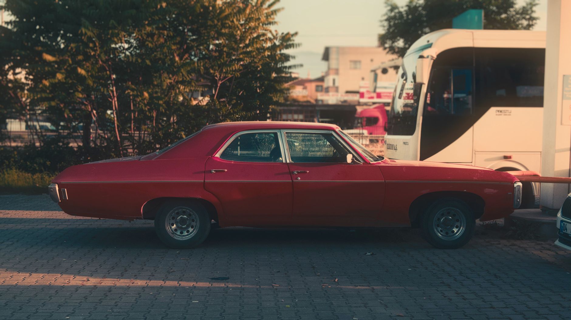 Classic red vintage car in city street setting with sunlight and trees.