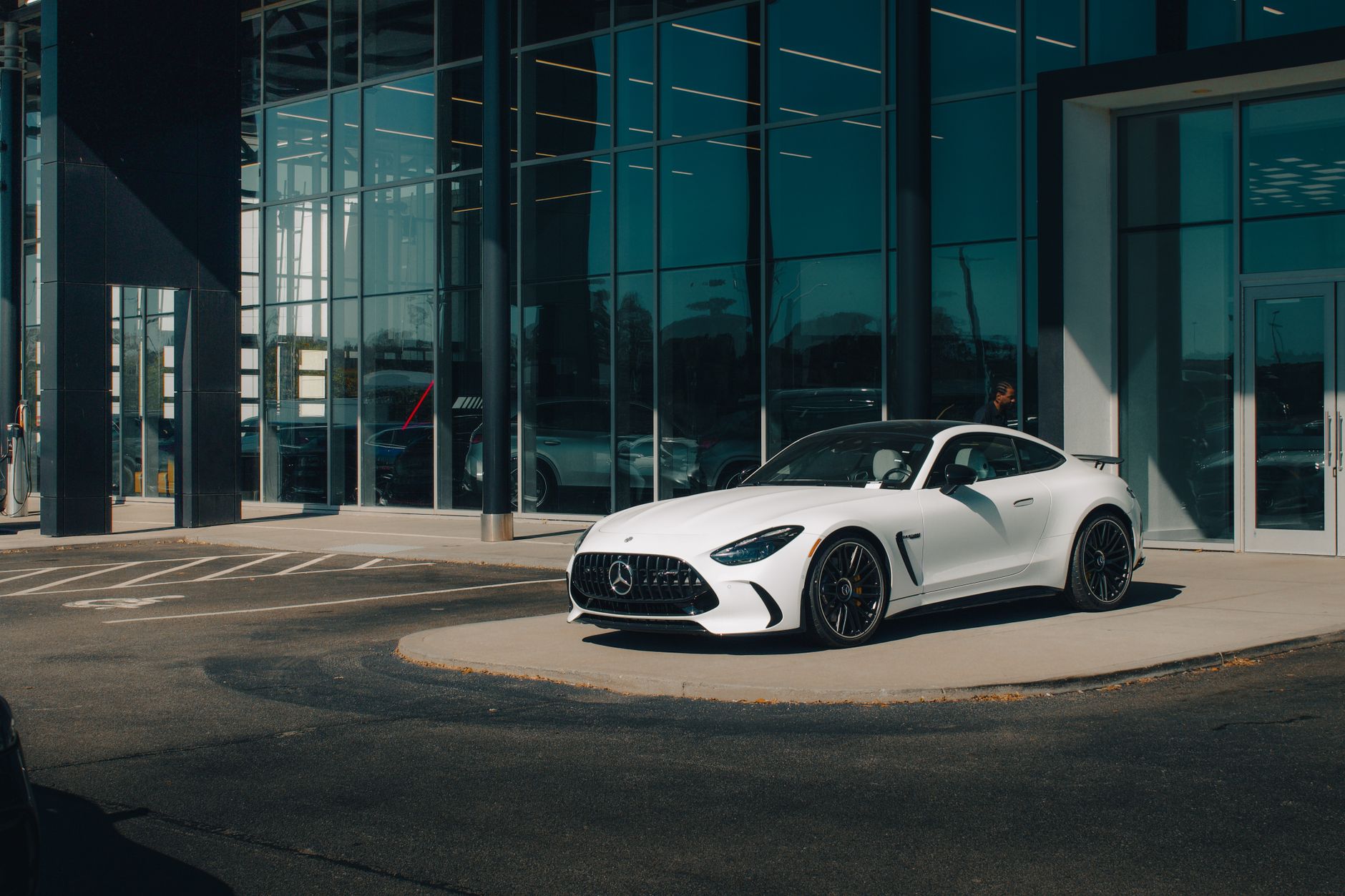 White Mercedes Benz sports car in front of a modern dealership with glass windows.
