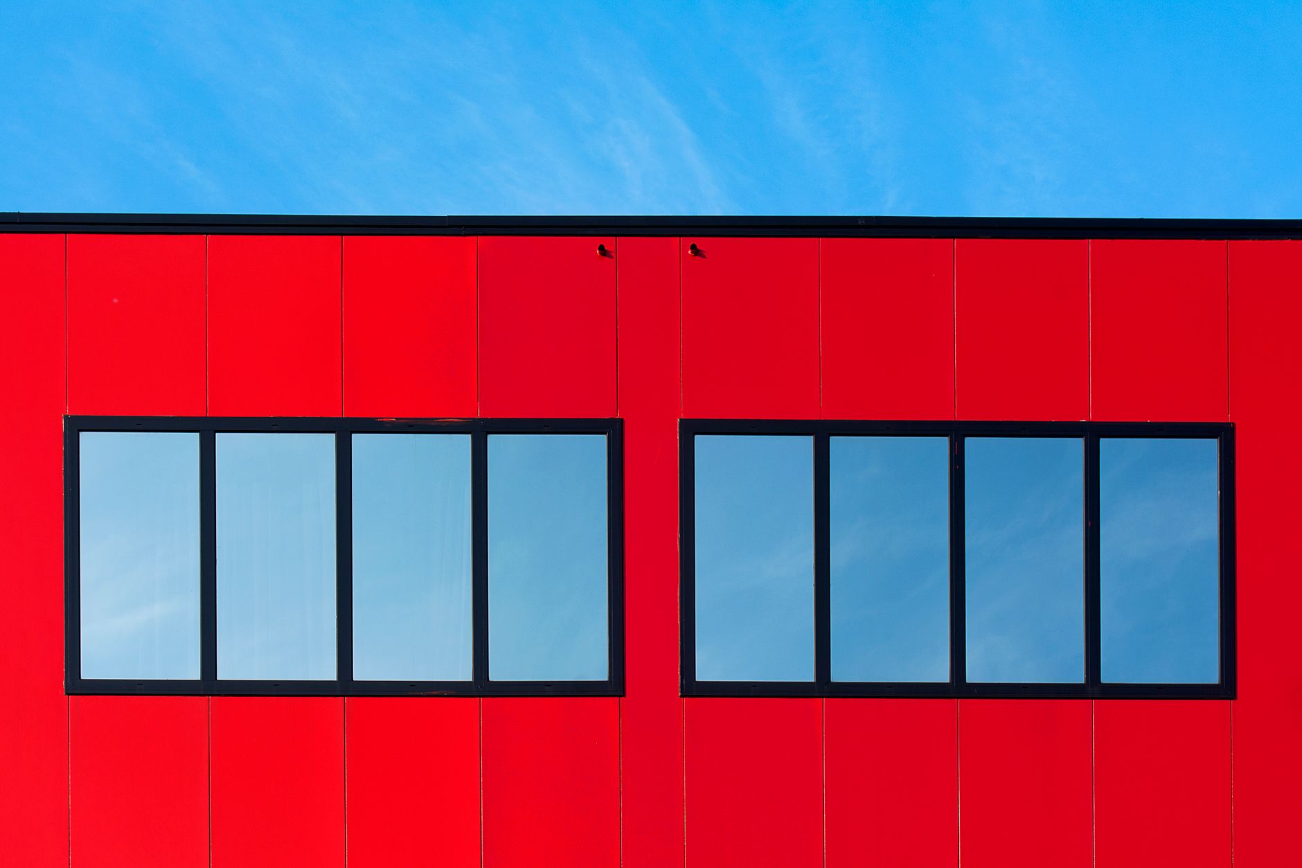 Minimalist red building facade with reflection of blue sky in glass windows.
