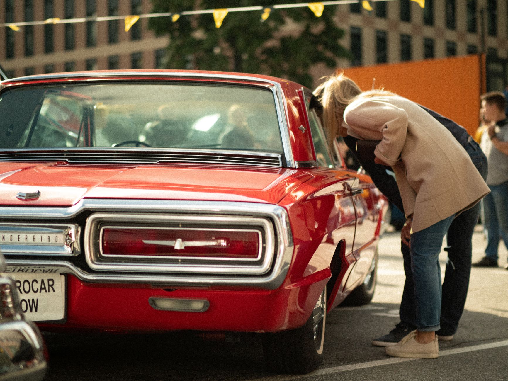 A classic red Thunderbird draws attention at an outdoor car show.