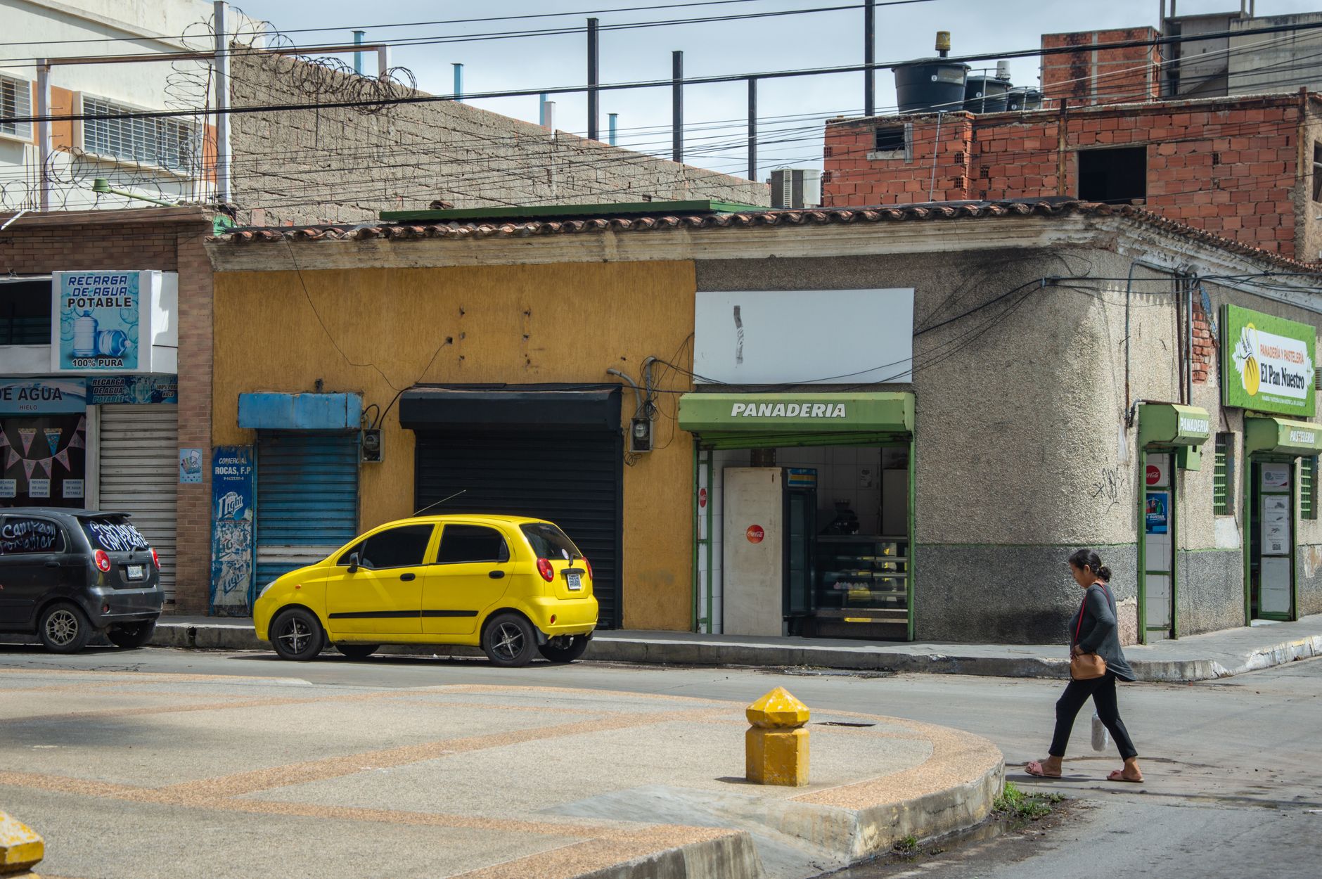 City street scene with a yellow car and panaderia, featuring urban architecture.