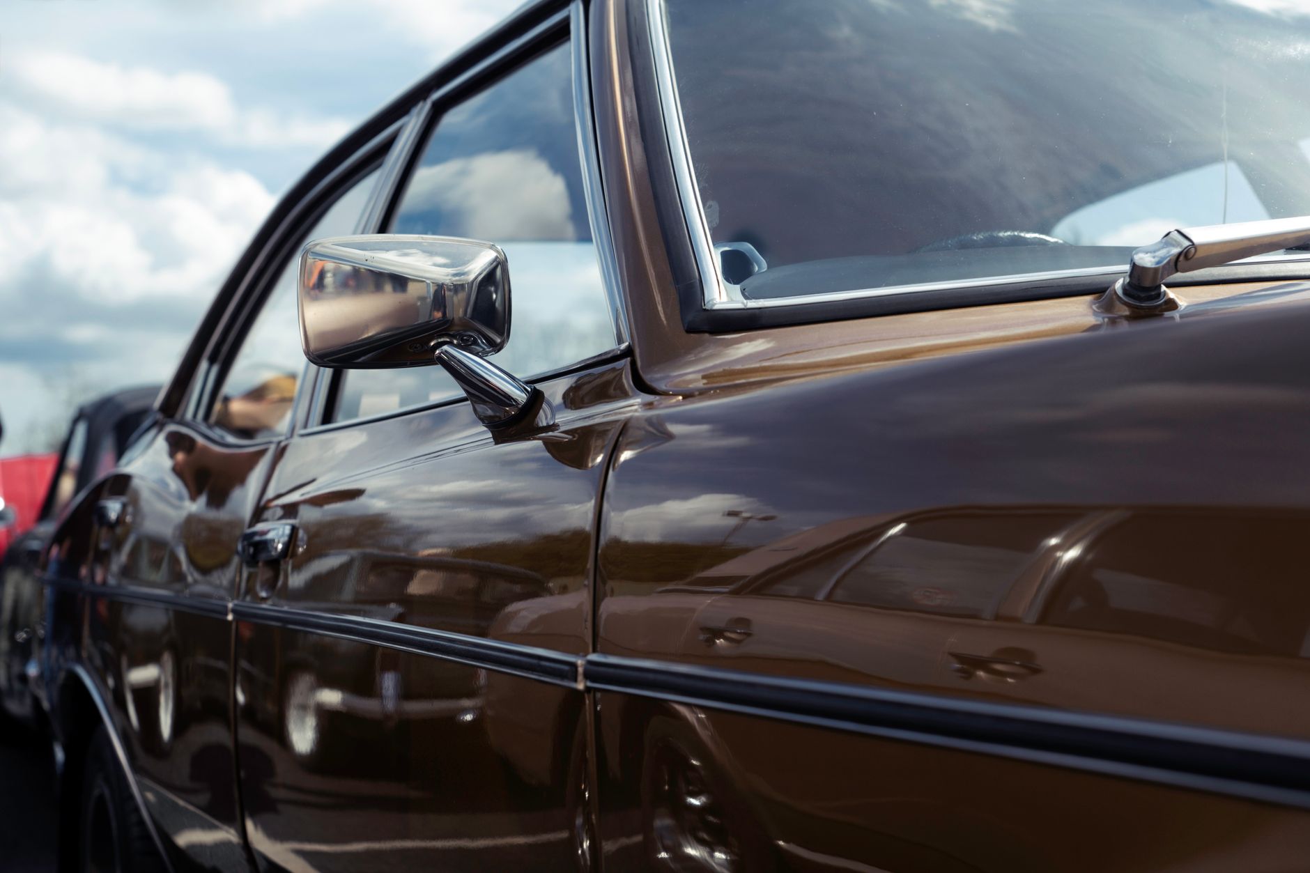 Close-up of a vintage car's glossy side with clear reflections on a sunny day.