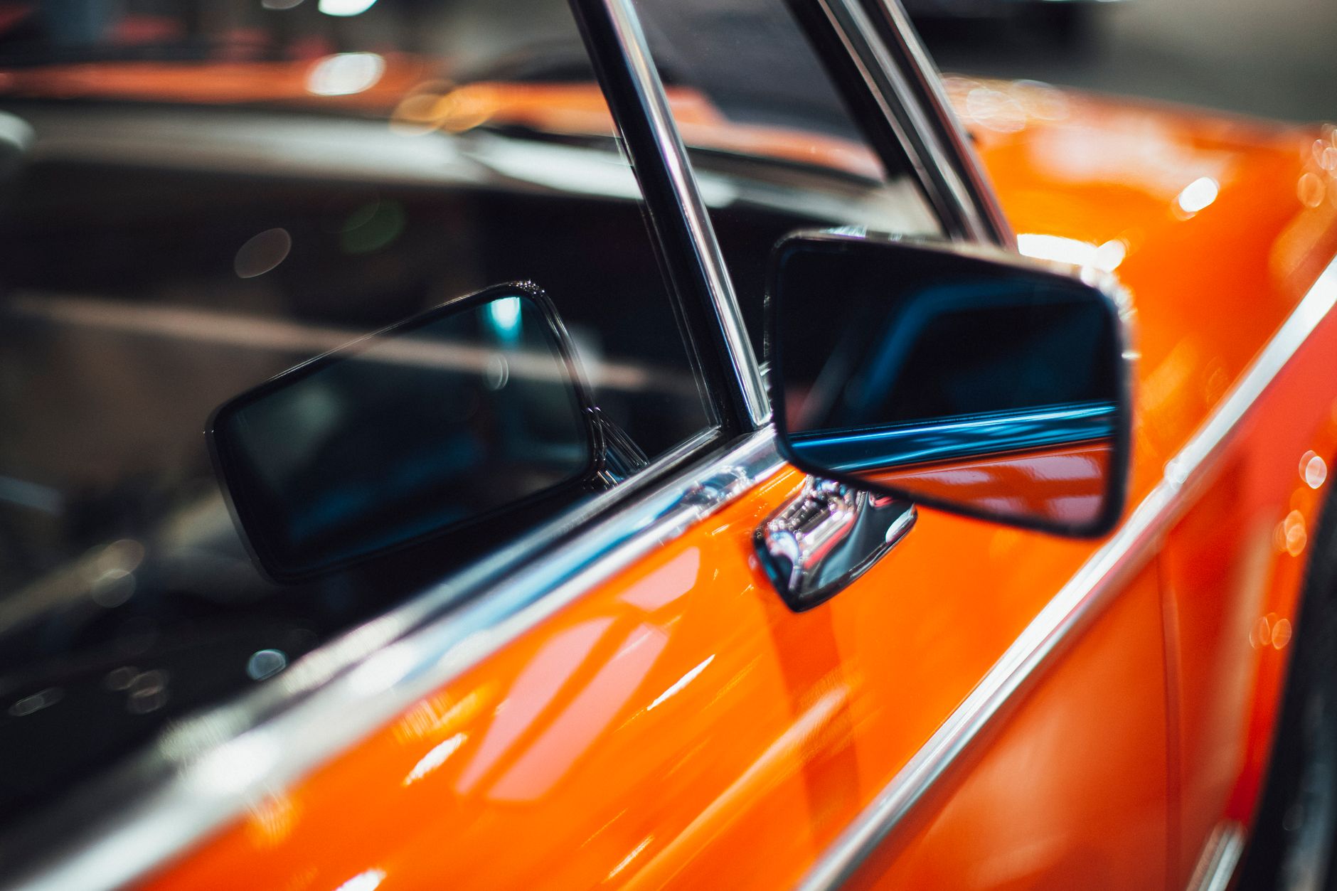 Side mirror and door of orange red old timer automobile glistening in electric lights of garage