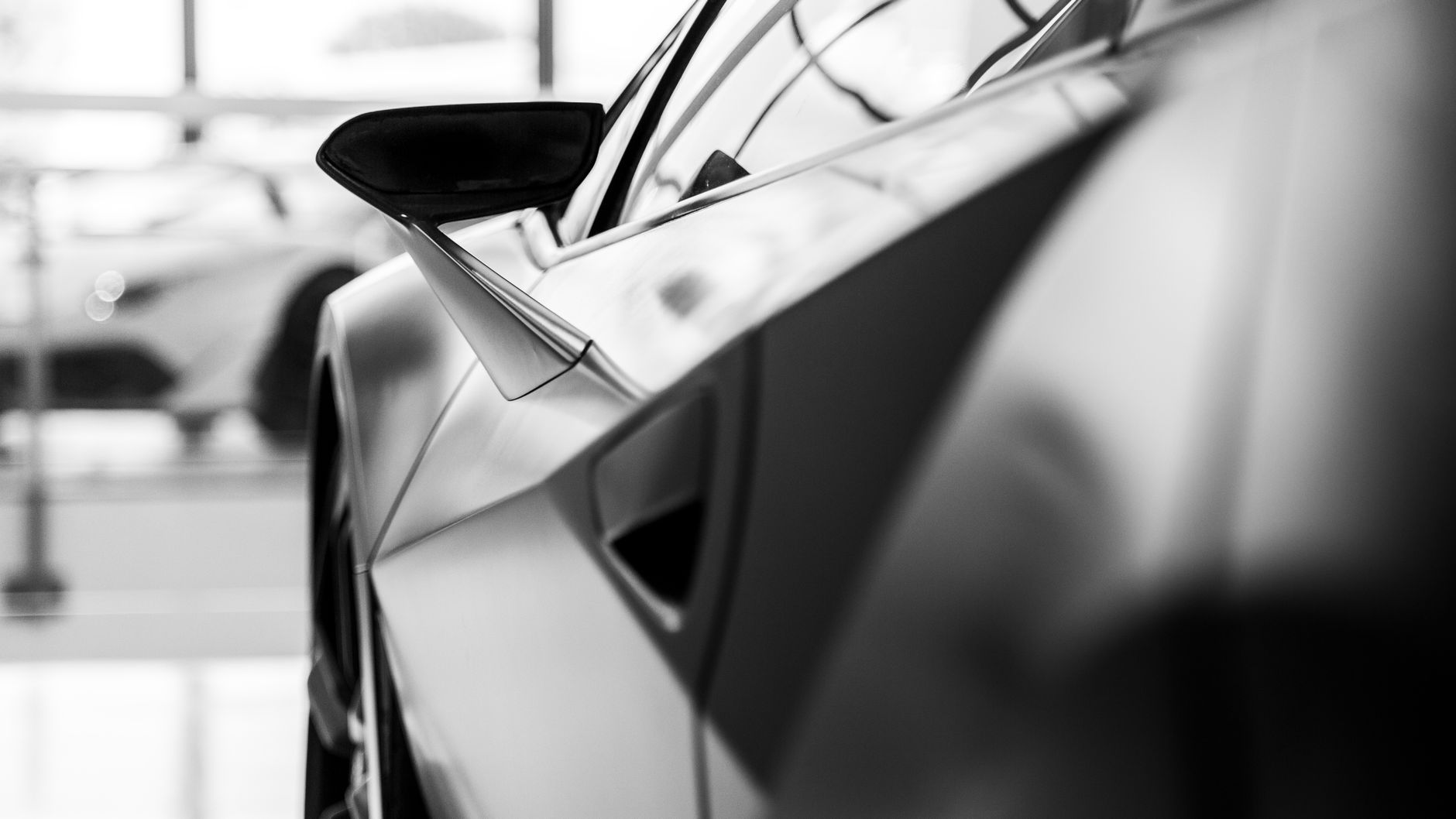 Stylish black and white close-up of a sports car's side mirror and design lines, emphasizing elegance.