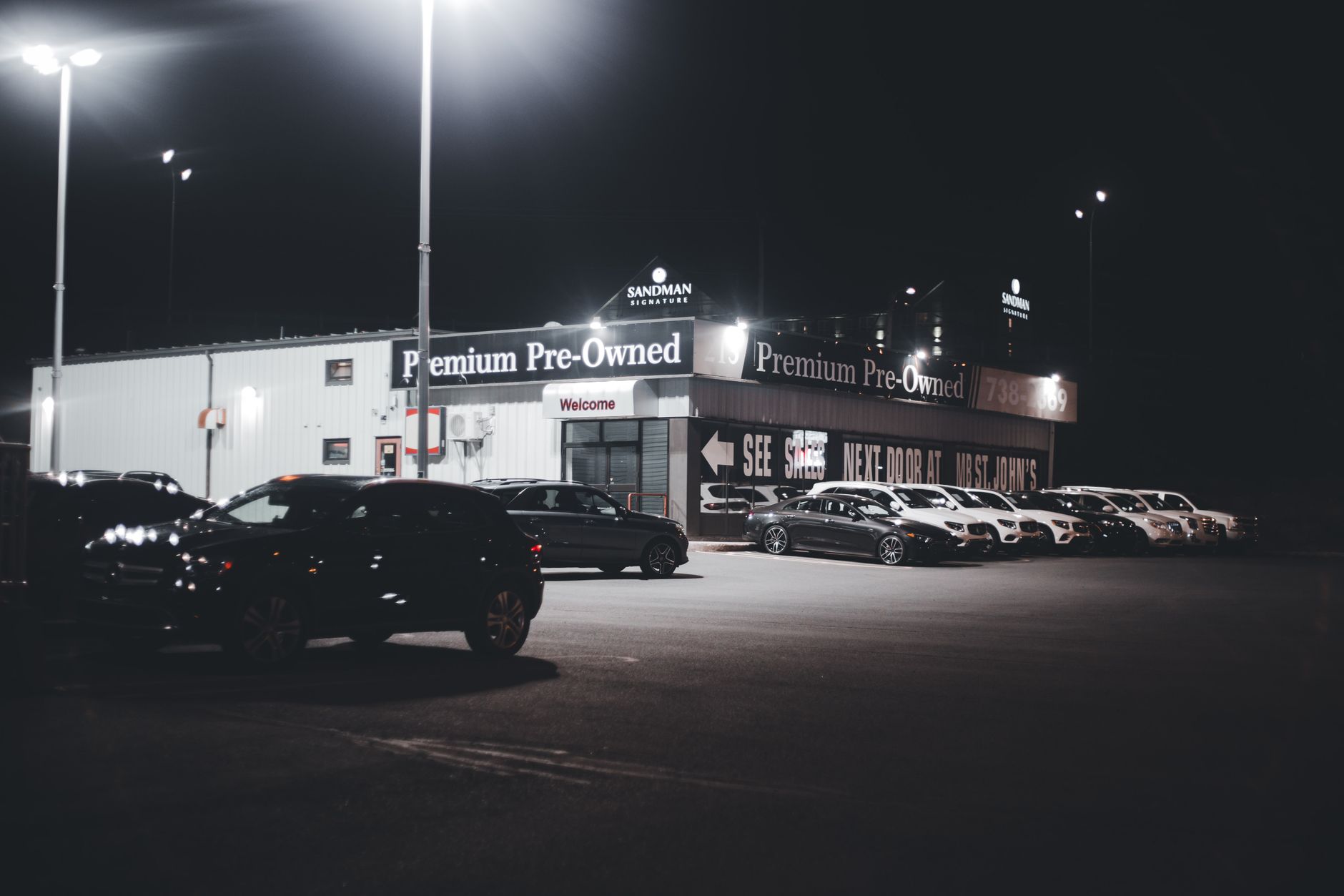 Illuminated car dealership lot showcasing premium pre-owned vehicles at night.